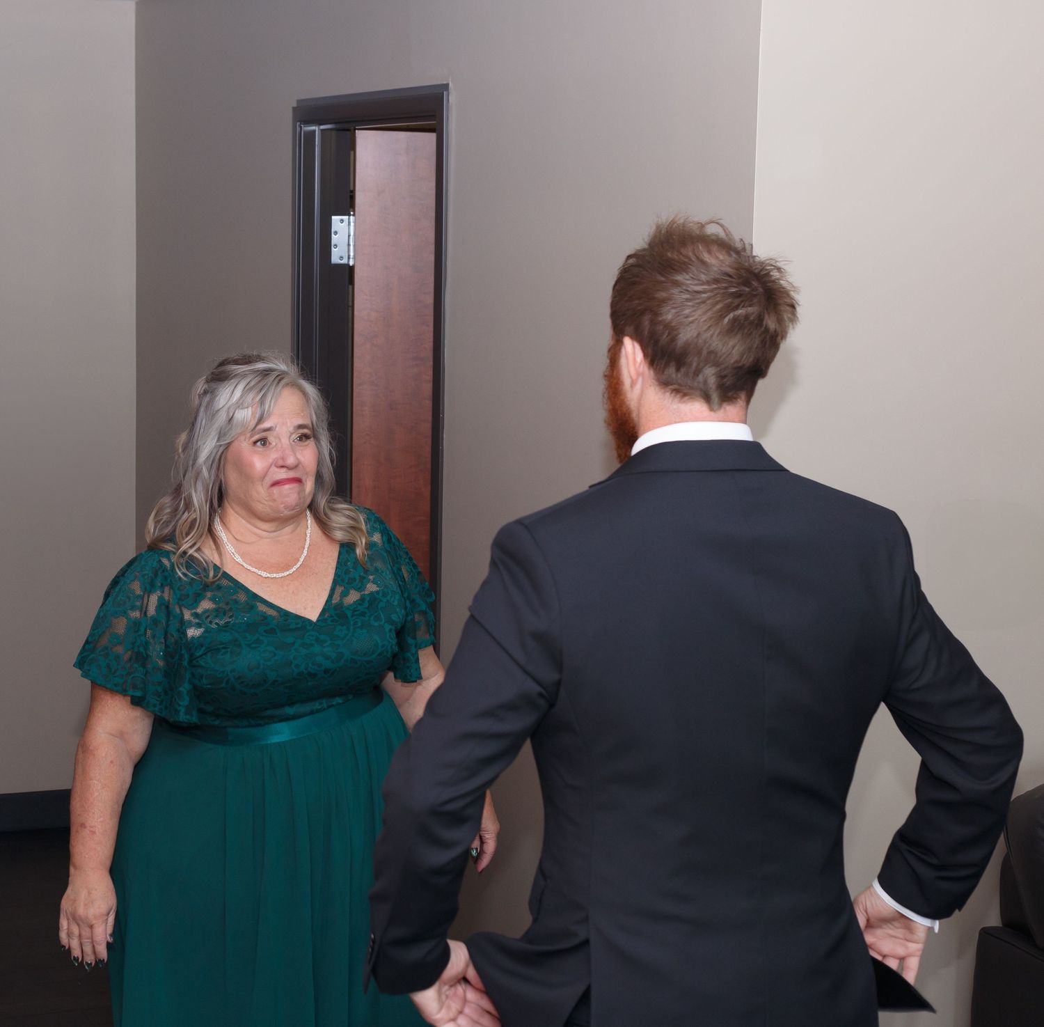 Wedding party members in emerald green dresses and dark suits interact in an indoor setting.