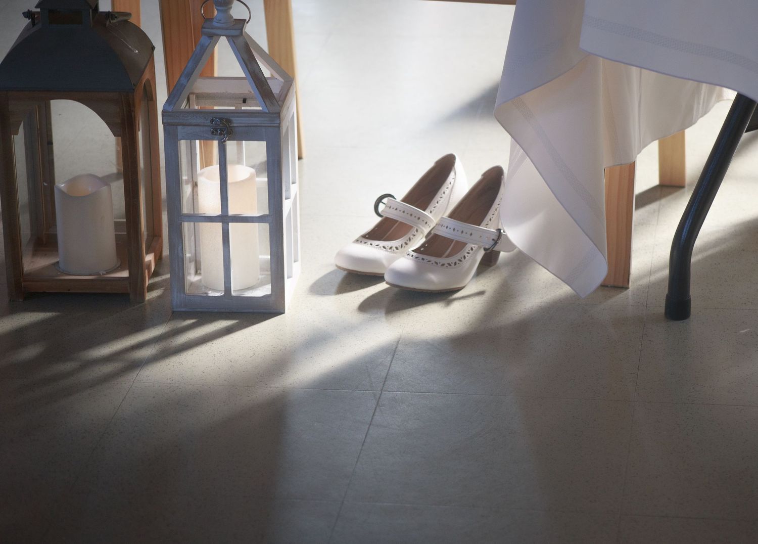 White bridal shoes placed near wooden lanterns in natural sunlight.