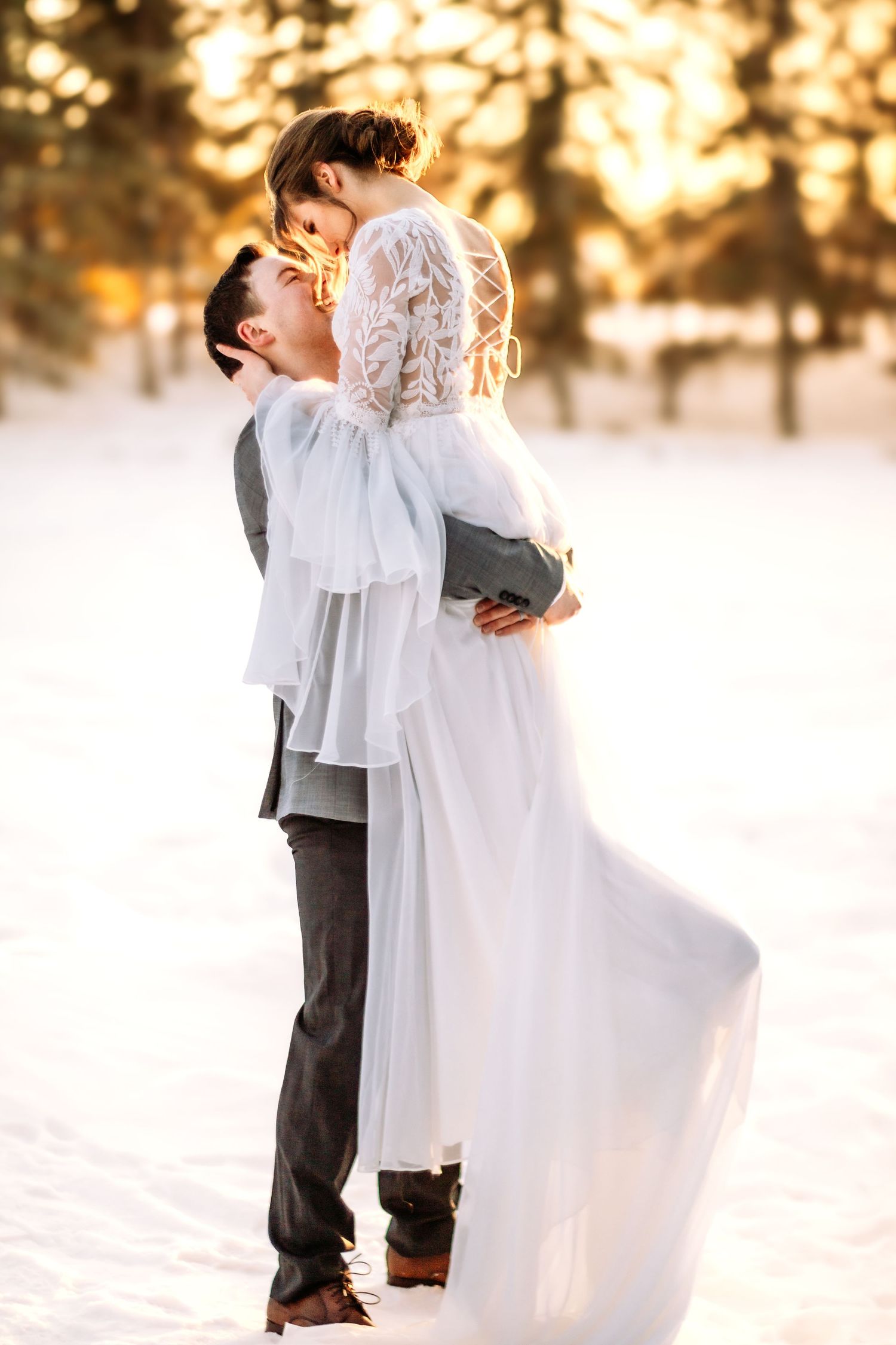 A romantic winter wedding photoshoot with the couple embracing in the snow at sunset.
