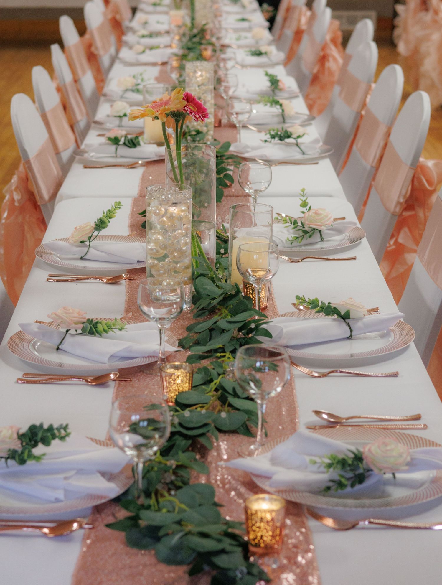 Elegant wedding reception table with white linens, greenery runners and glowing candles.