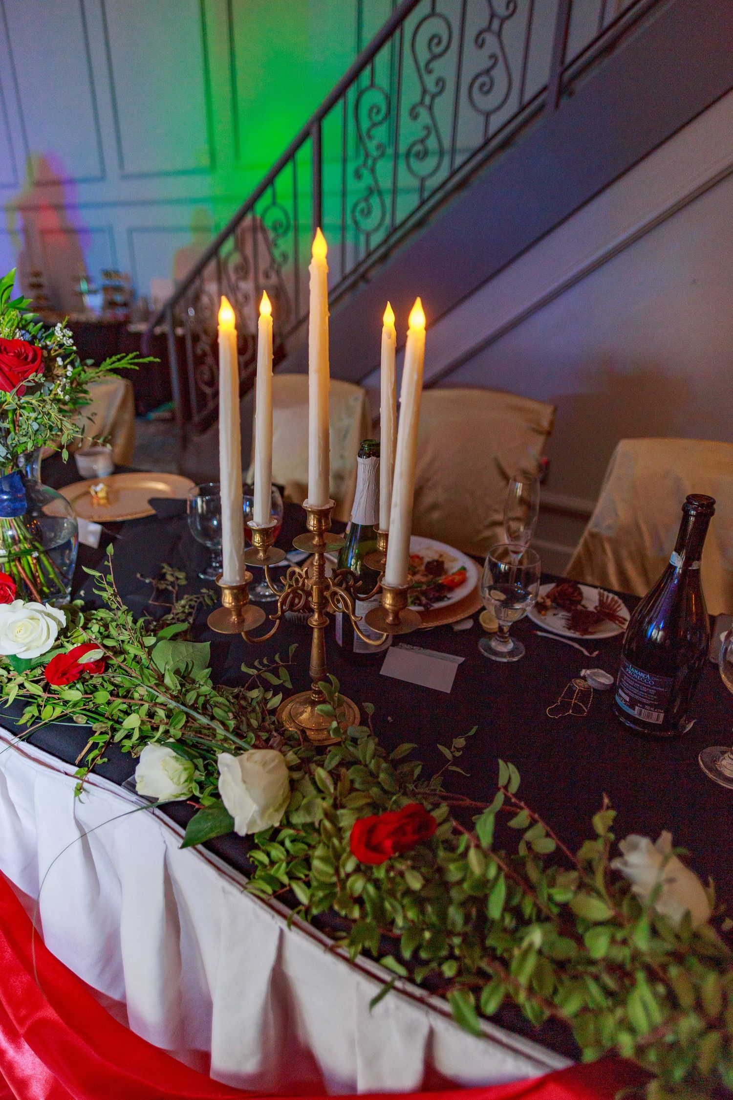 Elegant table setting with white candles, floral arrangements and decorative greenery.