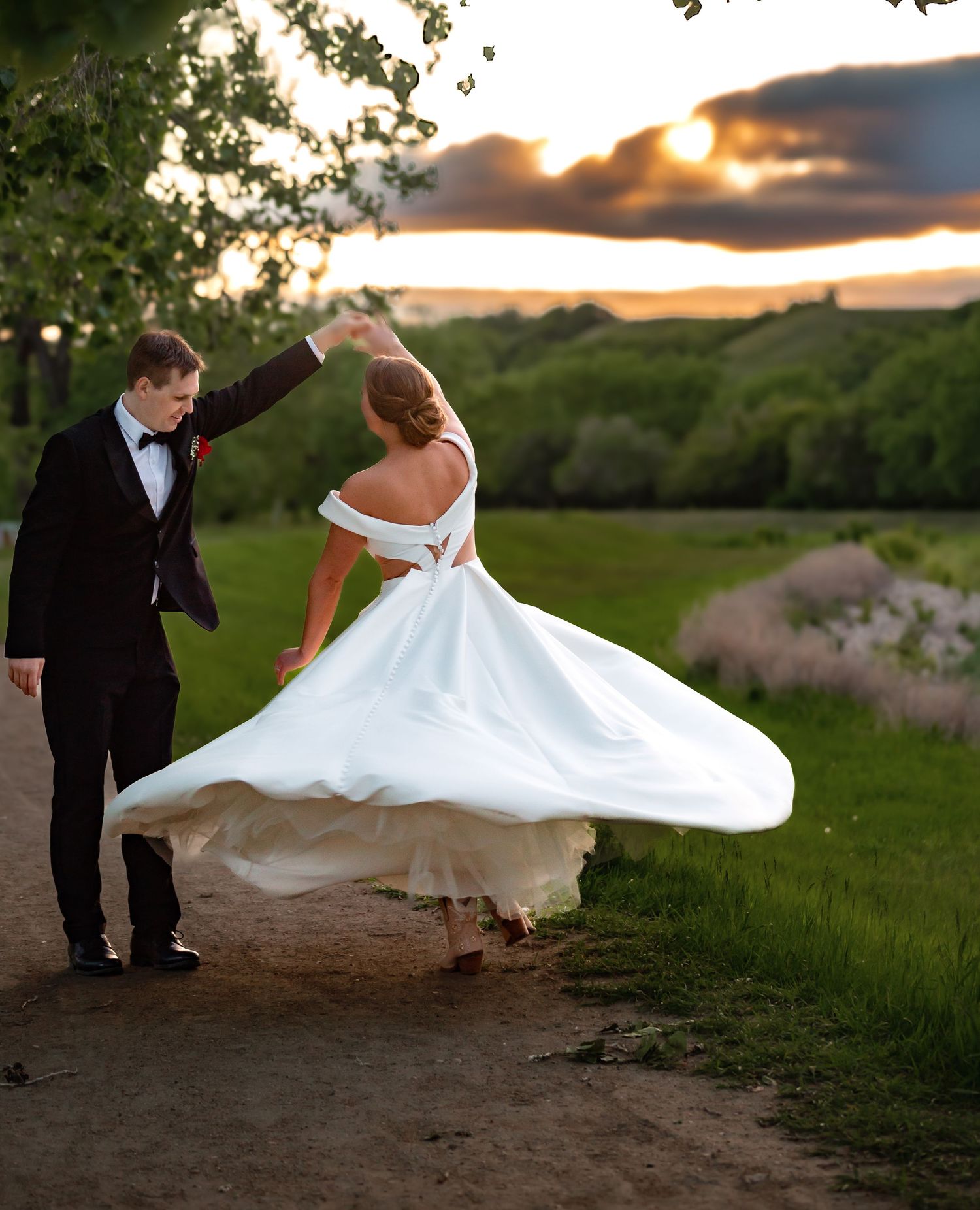 Wedding couple poses dramatically in a field at golden hour with dress billowing in the wind.