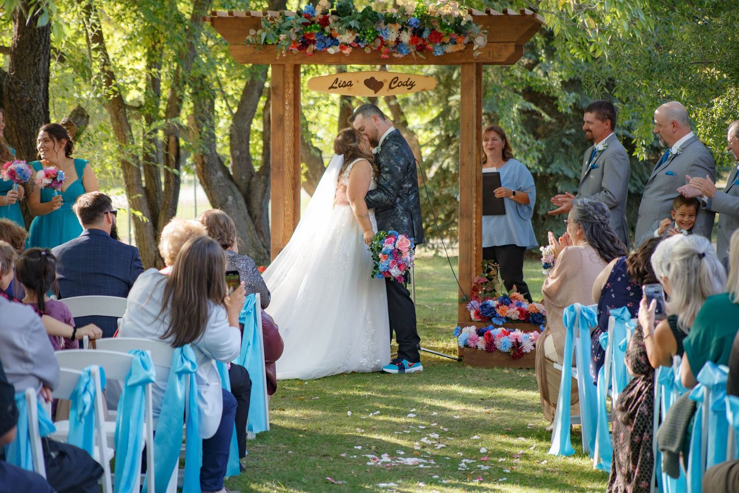Outdoor wedding ceremony setup with white chairs adorned with turquoise blue ribbons.