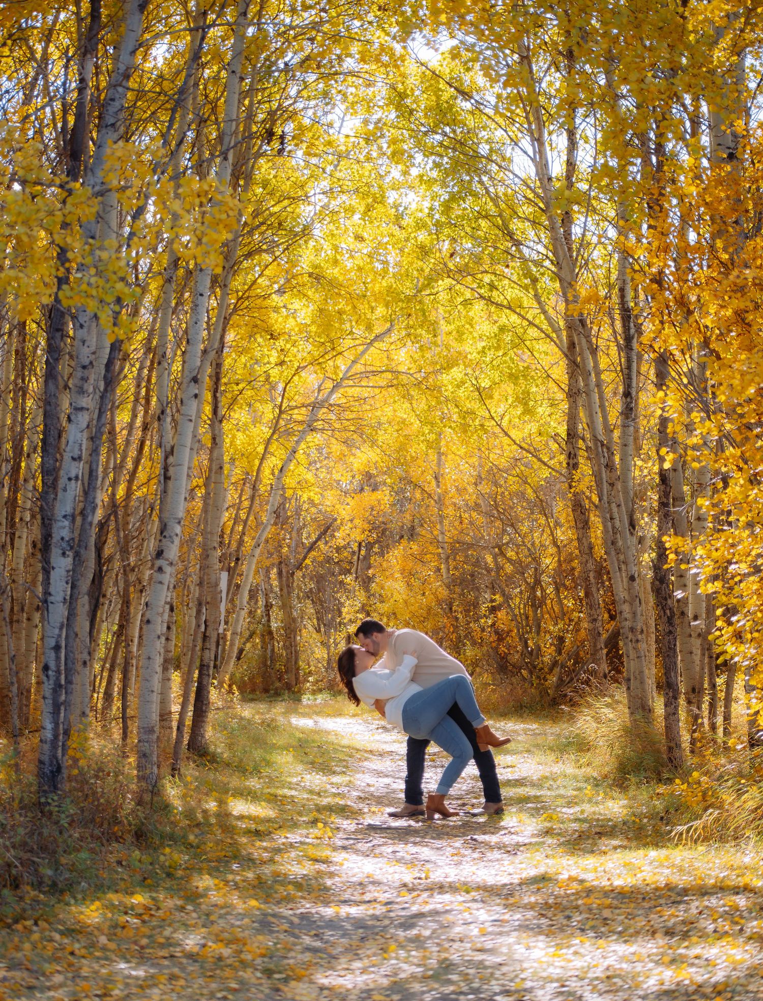 Romantic couple walking through a sunlit path lined with yellow autumn trees.