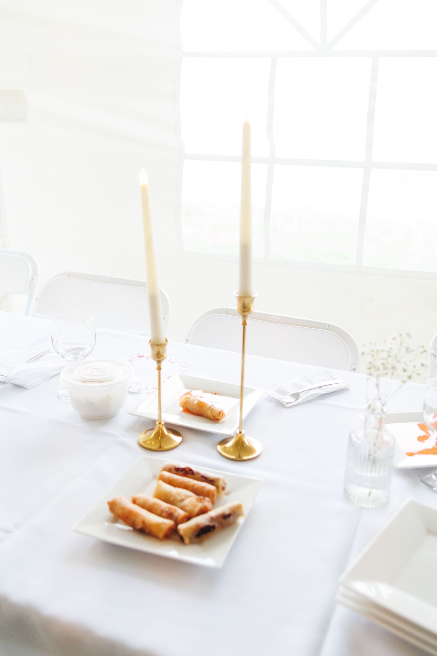 Elegant white wedding reception table setting with gold candles and minimalist place settings.