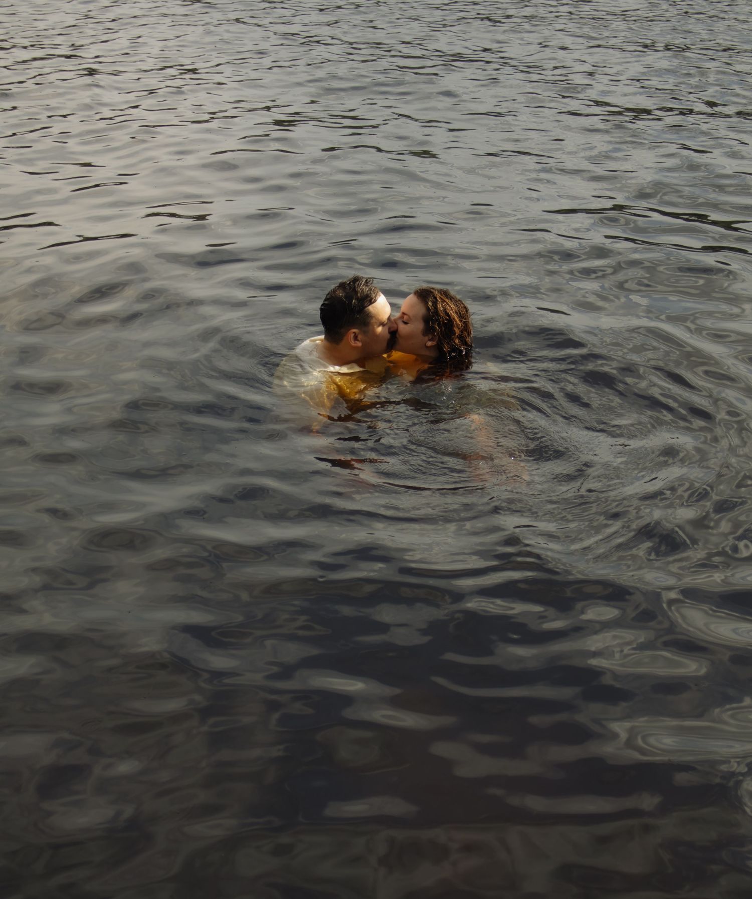 Two people swim together in dark rippling water.