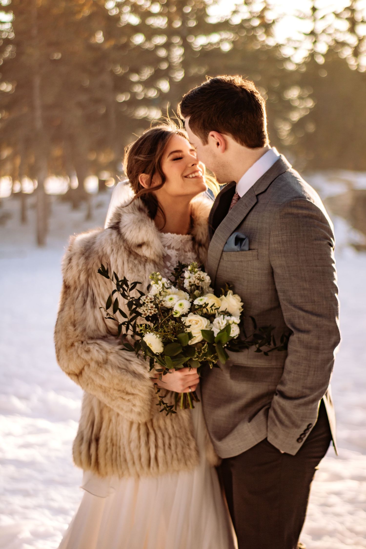 Winter wedding portrait with fur wrap and white bouquet in snowy setting.