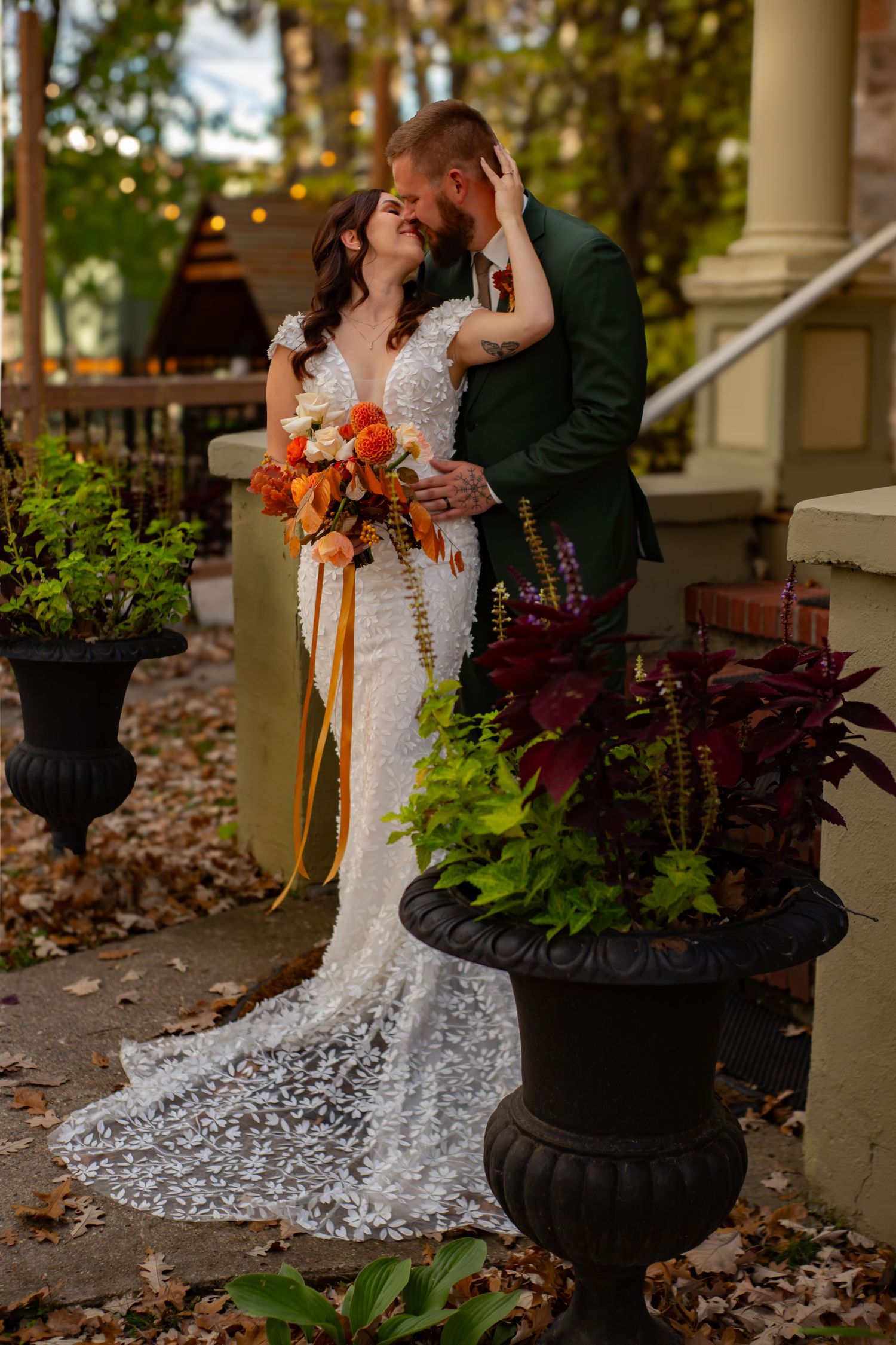 Wedding couple near decorative planters with autumn leaves scattered on porch.