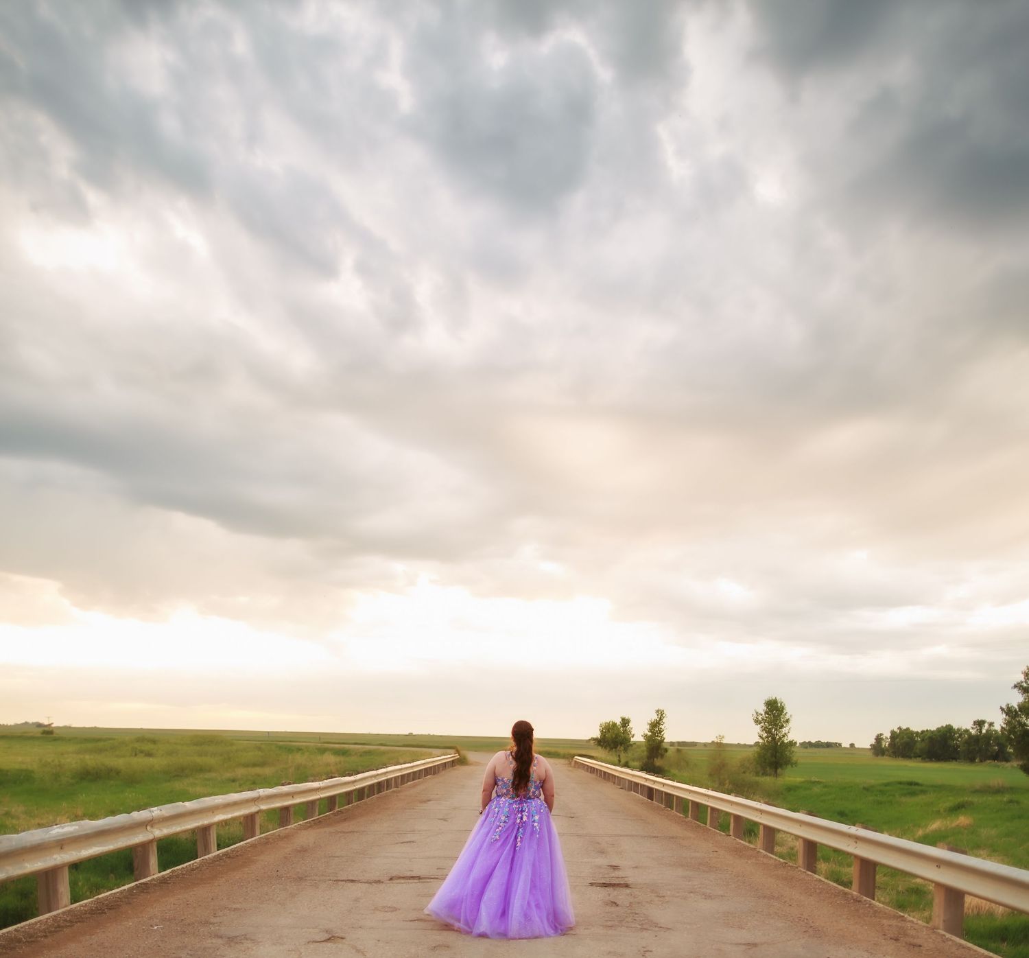A flowing purple dress creates a dramatic silhouette against a cloudy sky and open road.