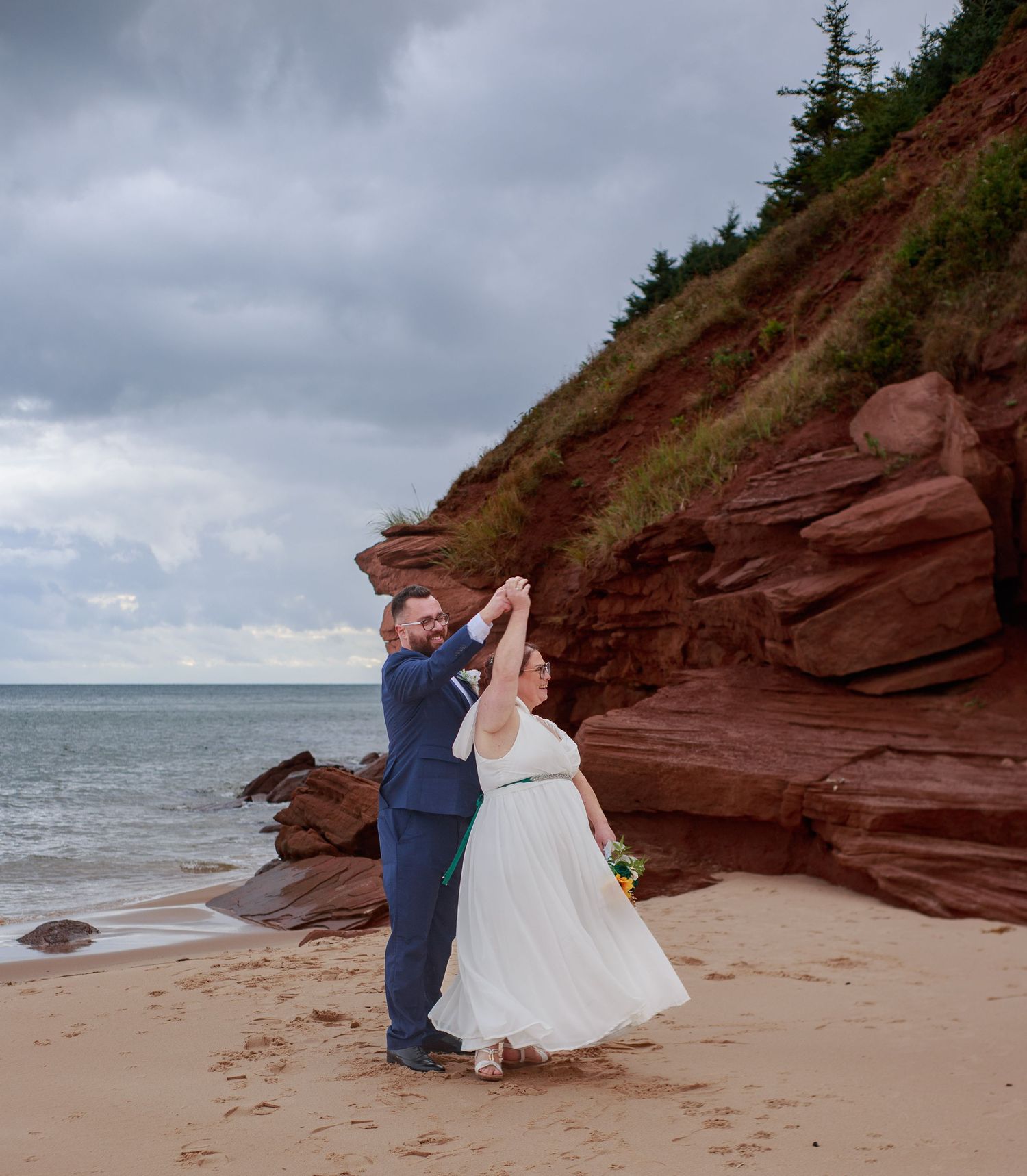 A romantic wedding photo session on a beach with red cliffs and dramatic cloudy skies in the background.