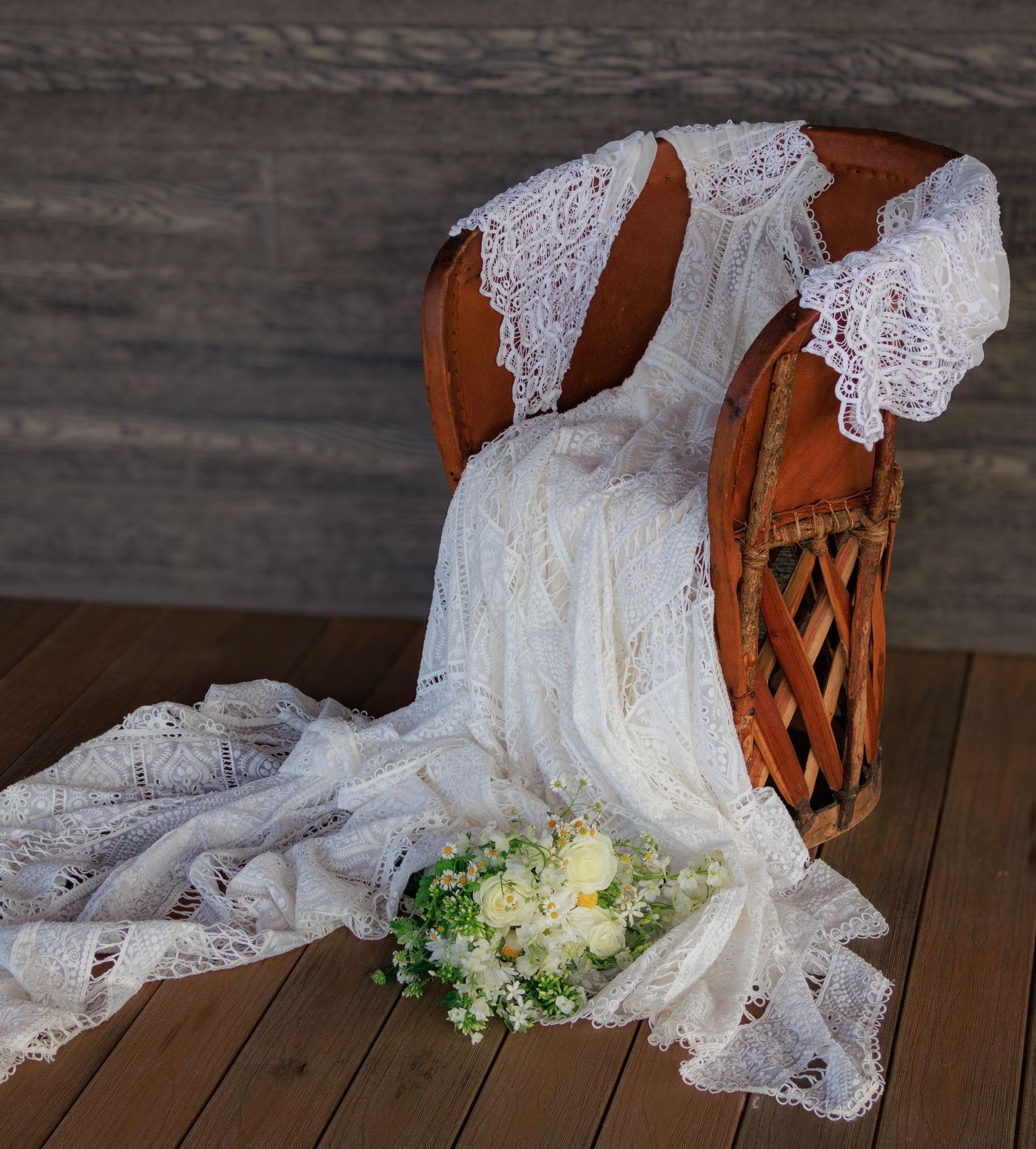 A delicate lace wedding dress and bouquet arranged on a rustic wooden deck.