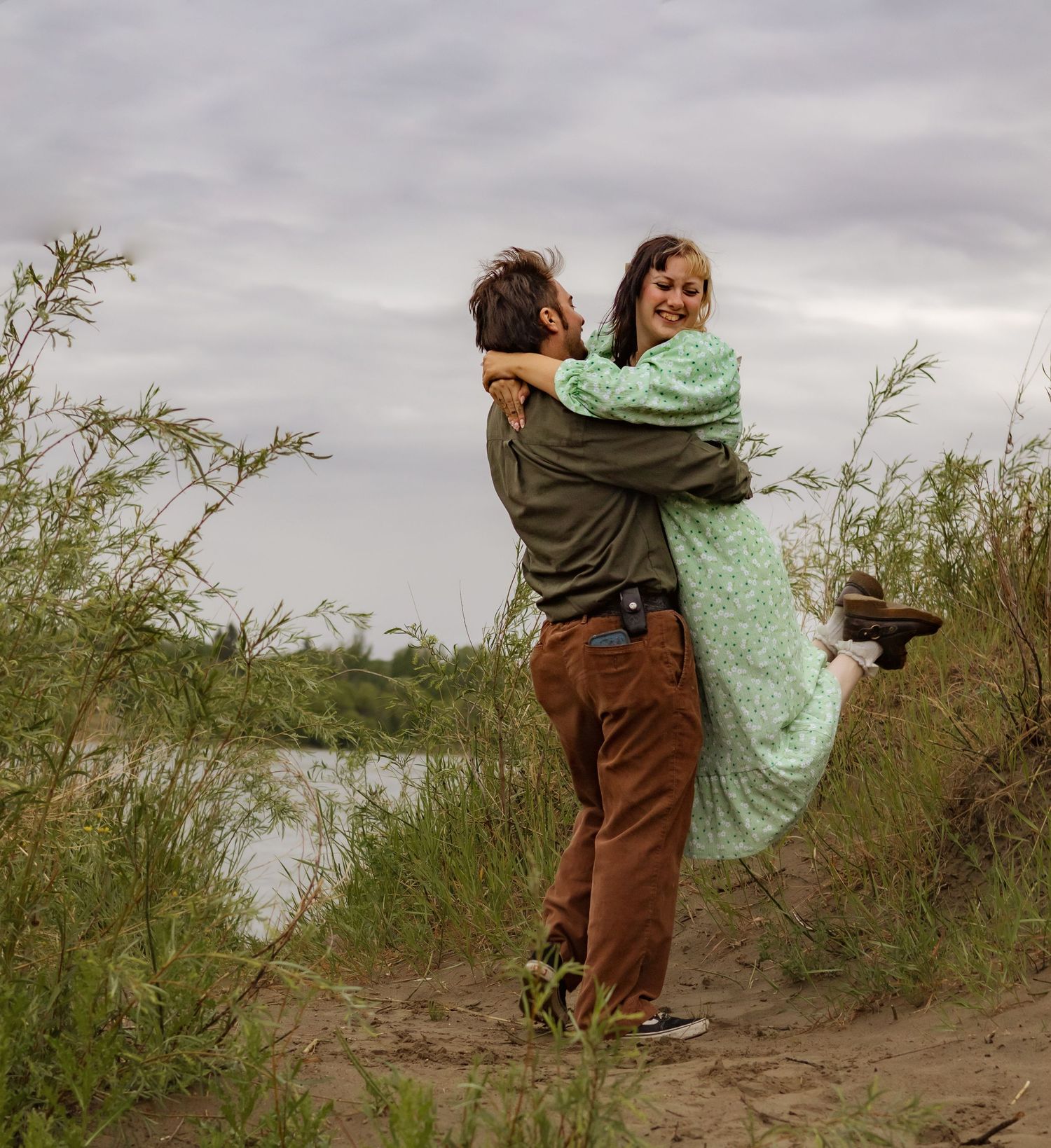 A couple in casual attire shares playful moments on a sandy hill.