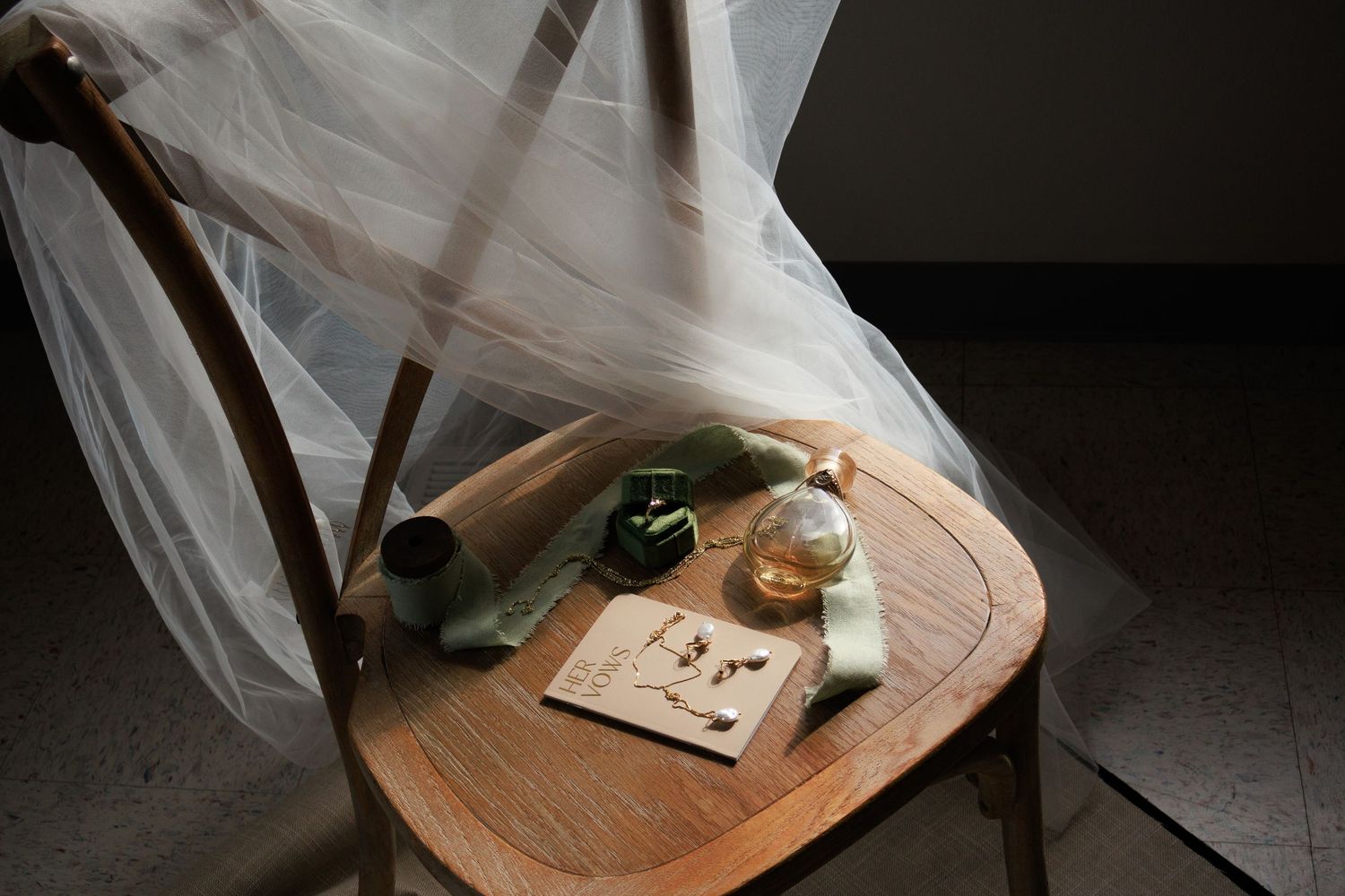 Minimalist wedding details with veil and rings on wooden surface in moody lighting.