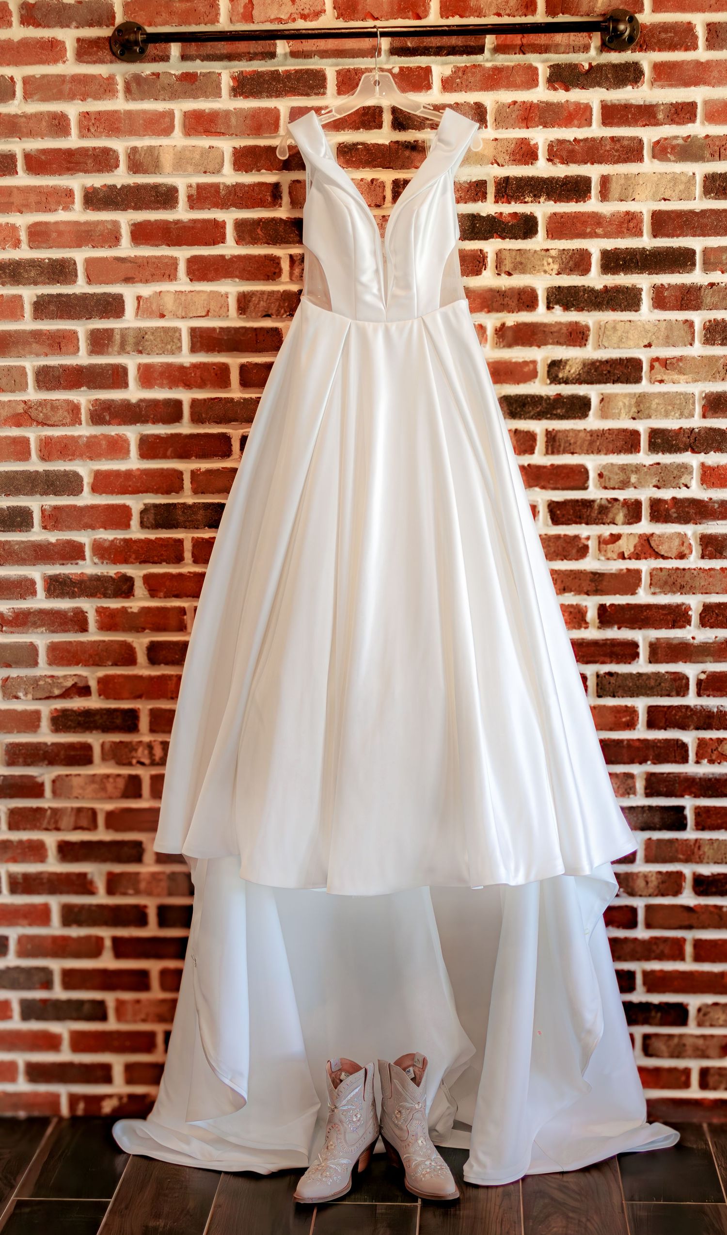 Elegant white wedding dress displayed against a rustic brick wall backdrop.
