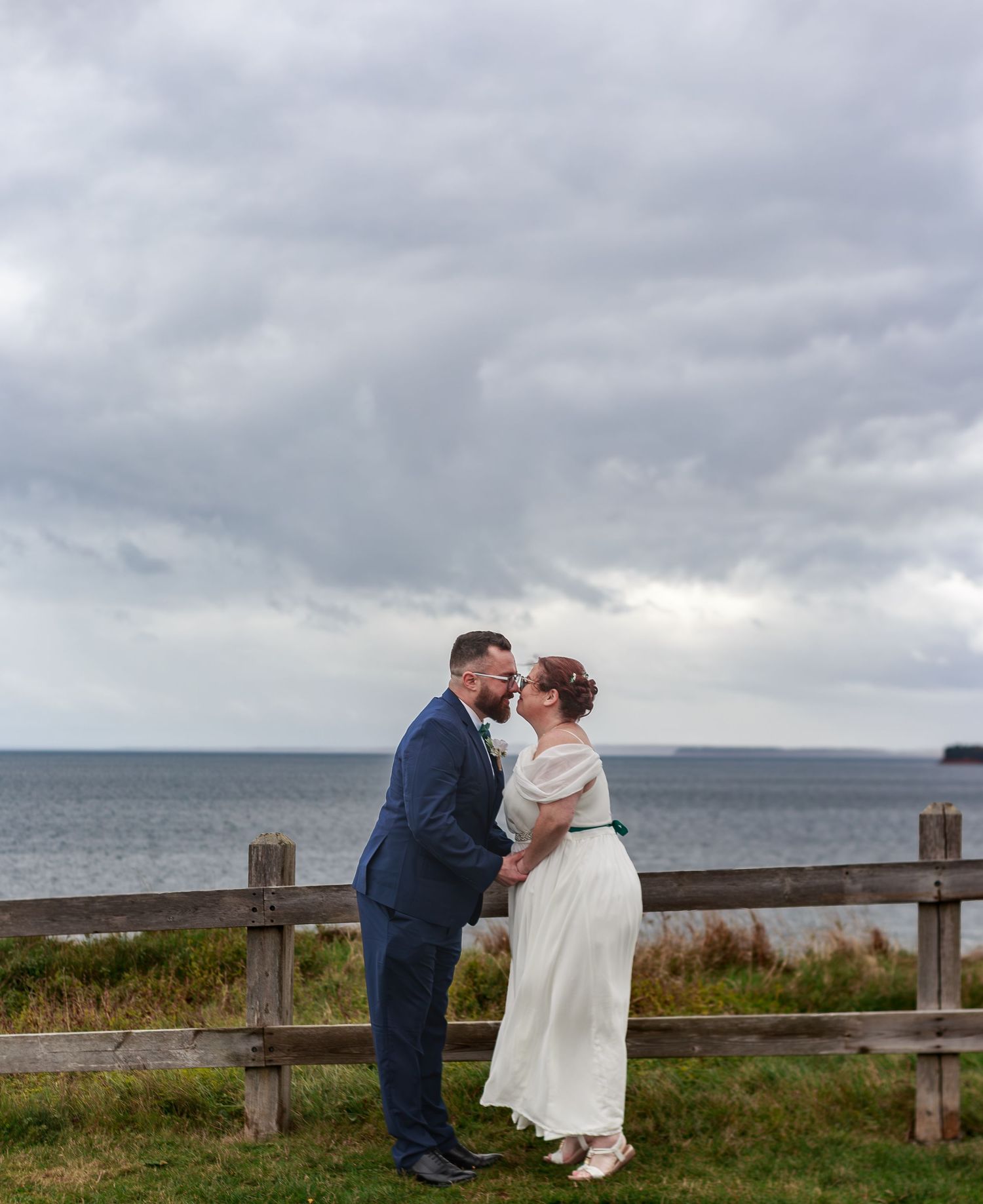 Couple sharing an intimate moment against a cloudy coastal backdrop.