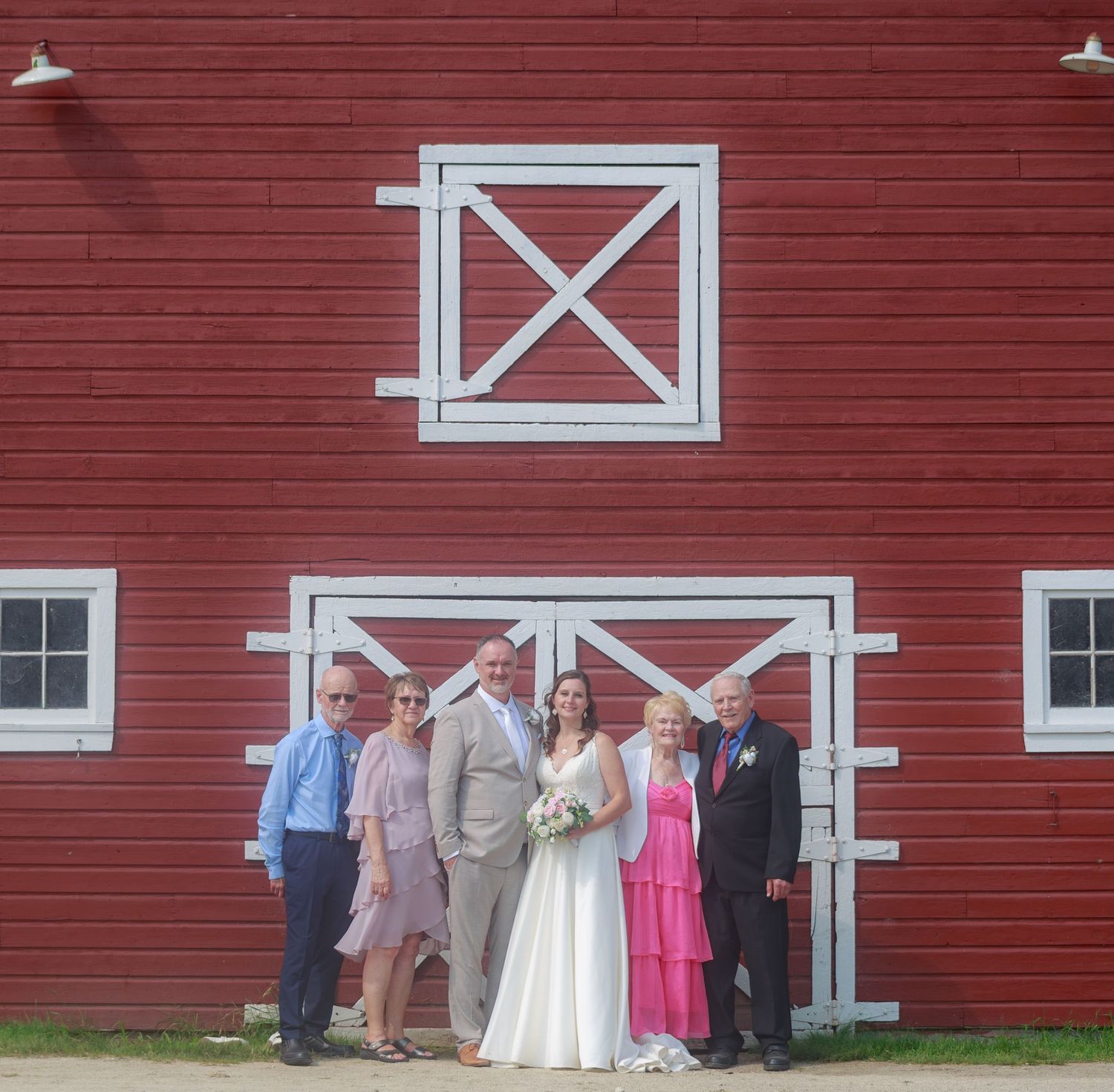 Wedding guests gathered outside a red barn with white trim during a summer celebration.