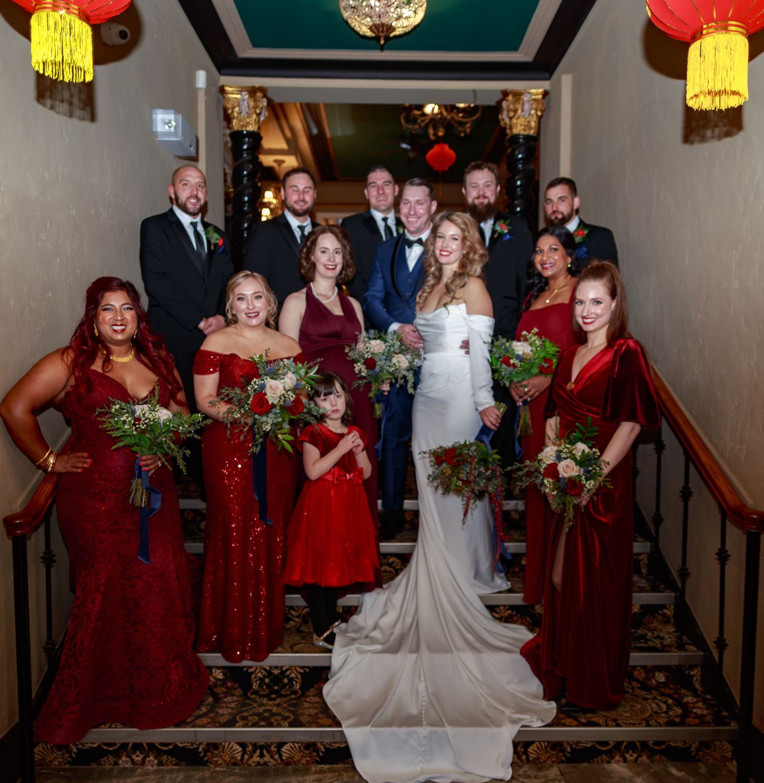 Wedding party members in burgundy dresses pose with the bride in a white gown against an elegant backdrop.