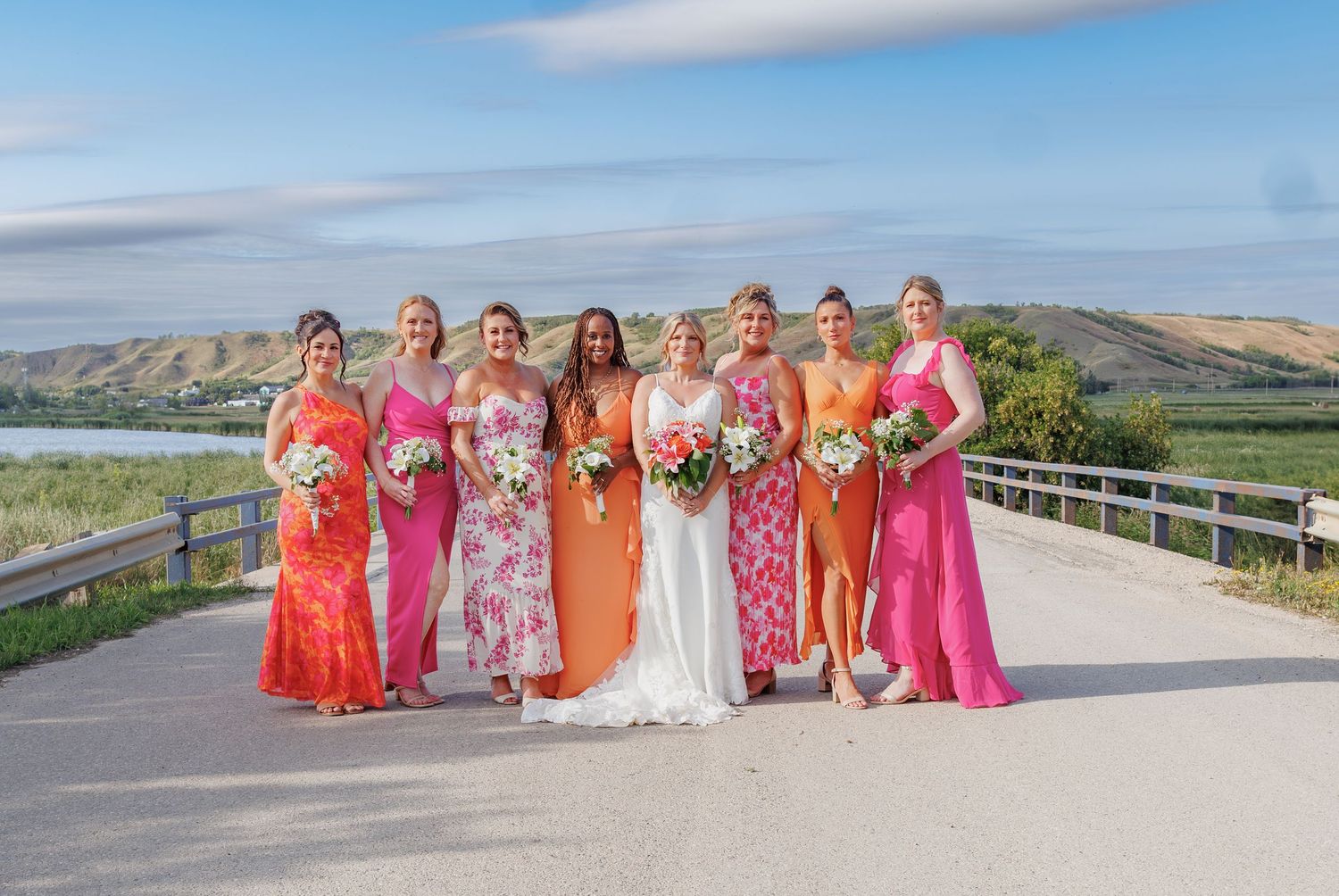 Wedding party in vibrant coral and orange dresses posing against scenic mountain backdrop.