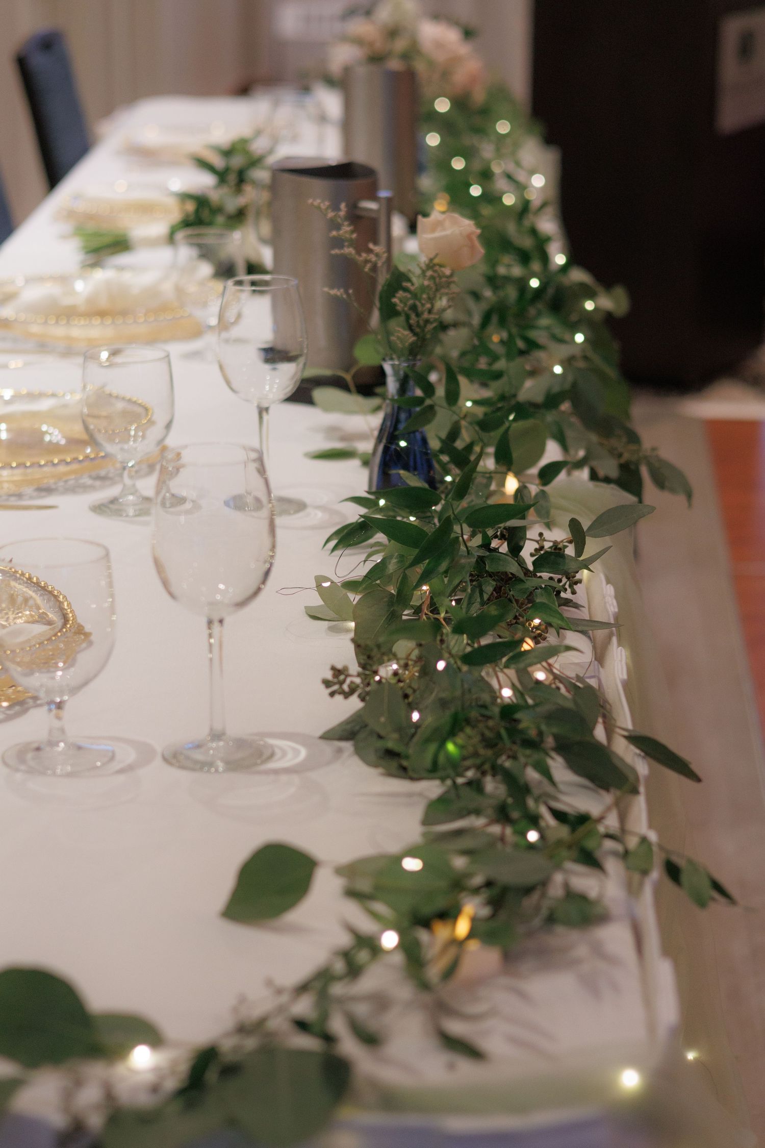 Elegant wedding table decor with twinkling lights and green foliage arrangements.