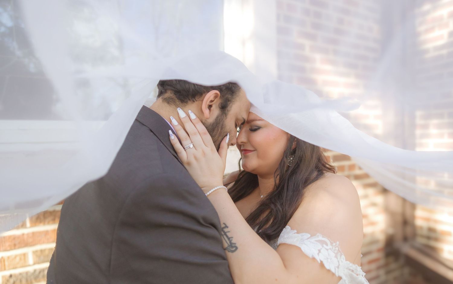 An intimate wedding moment captured under flowing white veil with soft lighting.