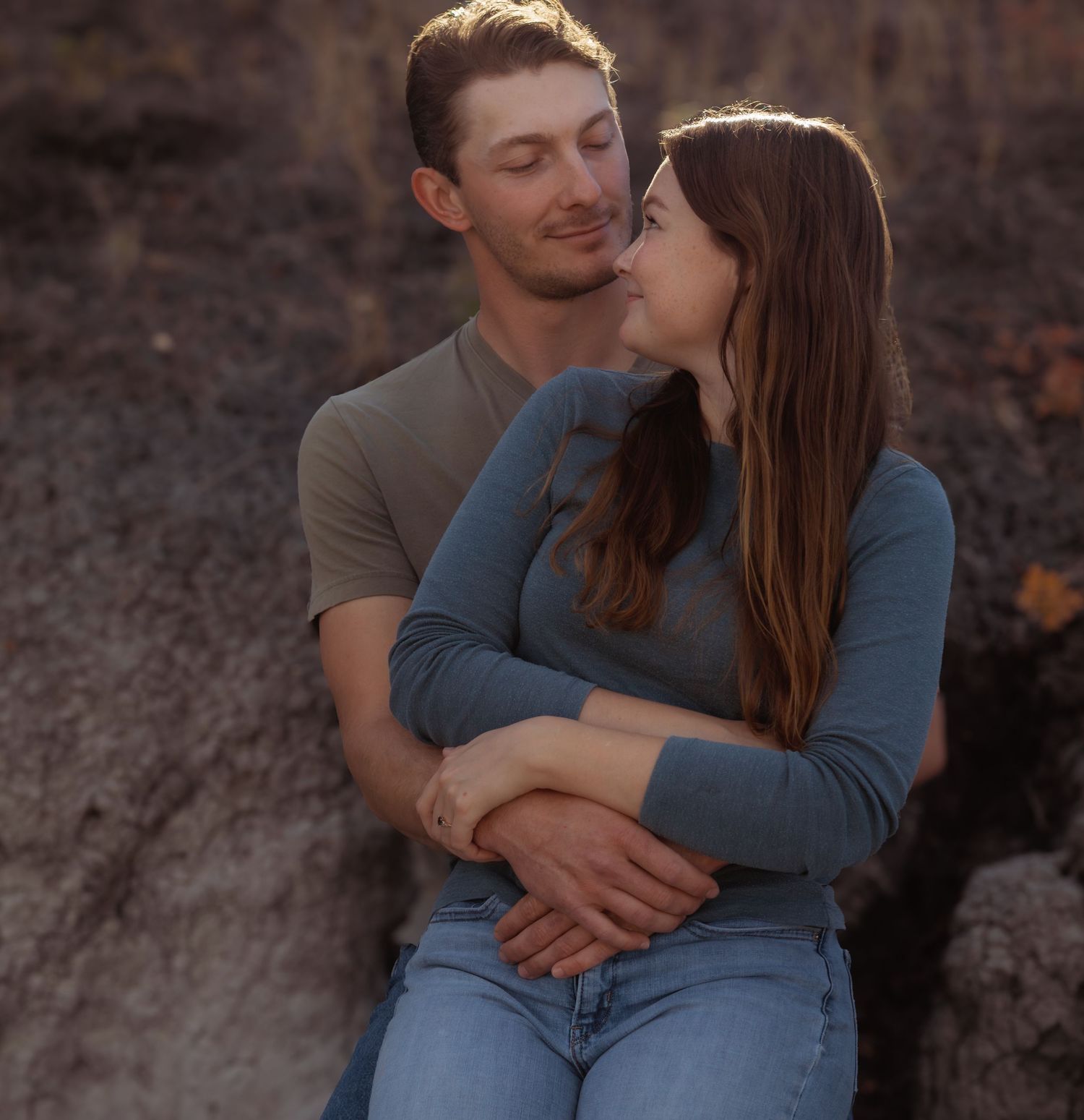 Tender moments between couple sitting on rocks during sunset.