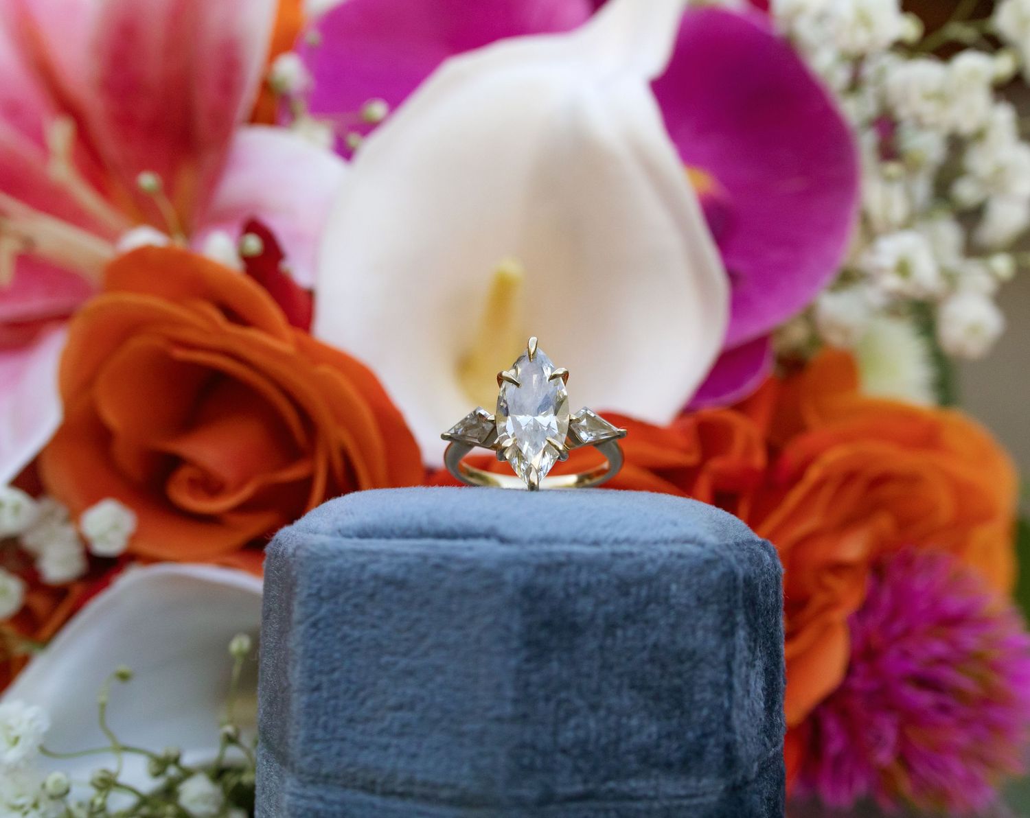 Vibrant wedding bouquet with pink orchids, orange roses and white flowers arranged with a sparkling engagement ring.
