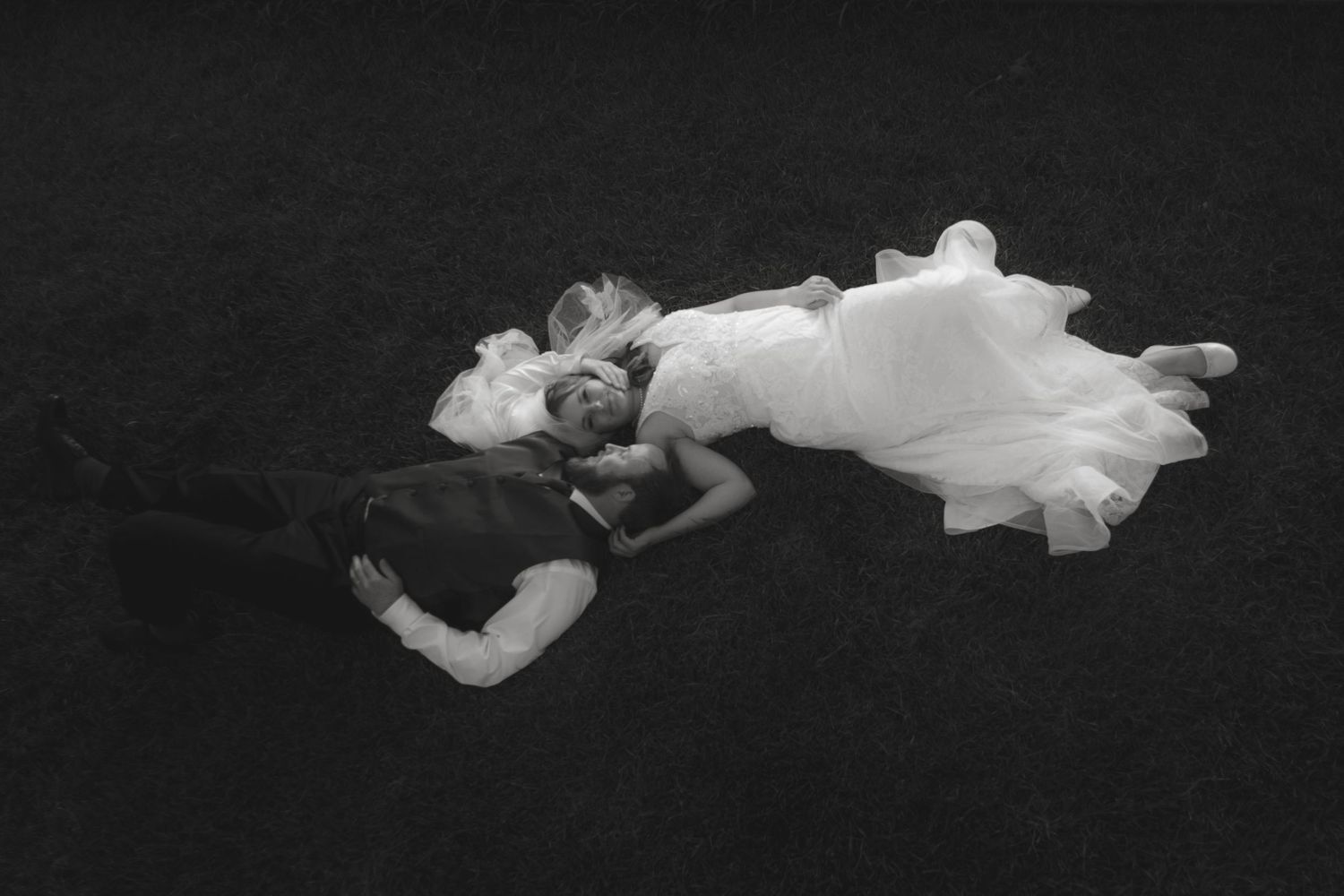 Artistic black and white photo of a figure in flowing white dress lying on dark background.