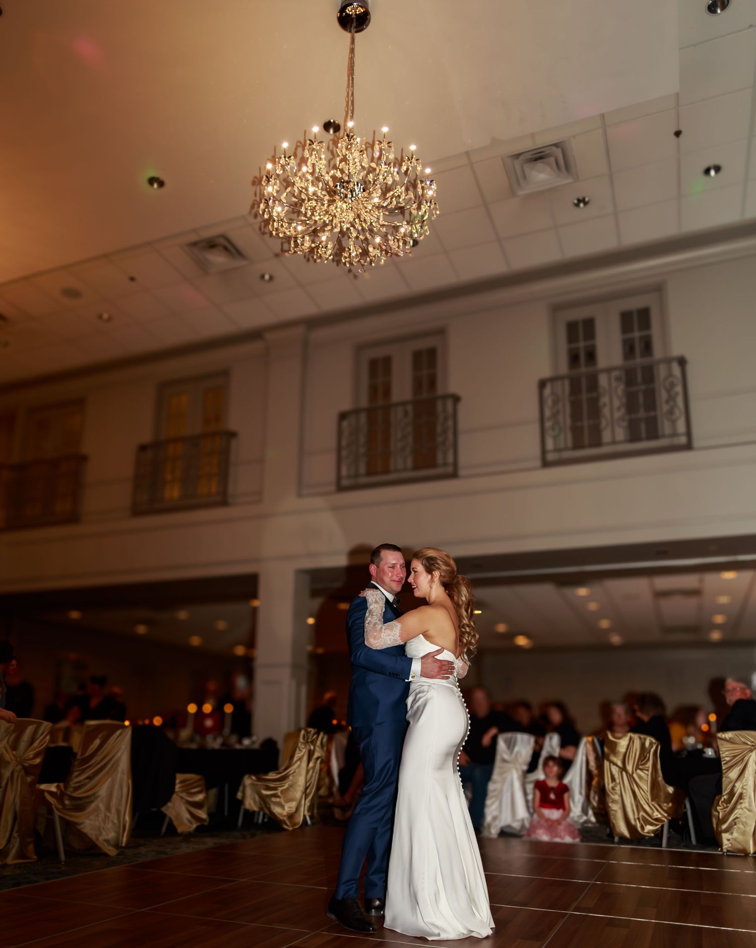 Elegant ballroom with crystal chandeliers and draped chairs set up for a wedding reception.