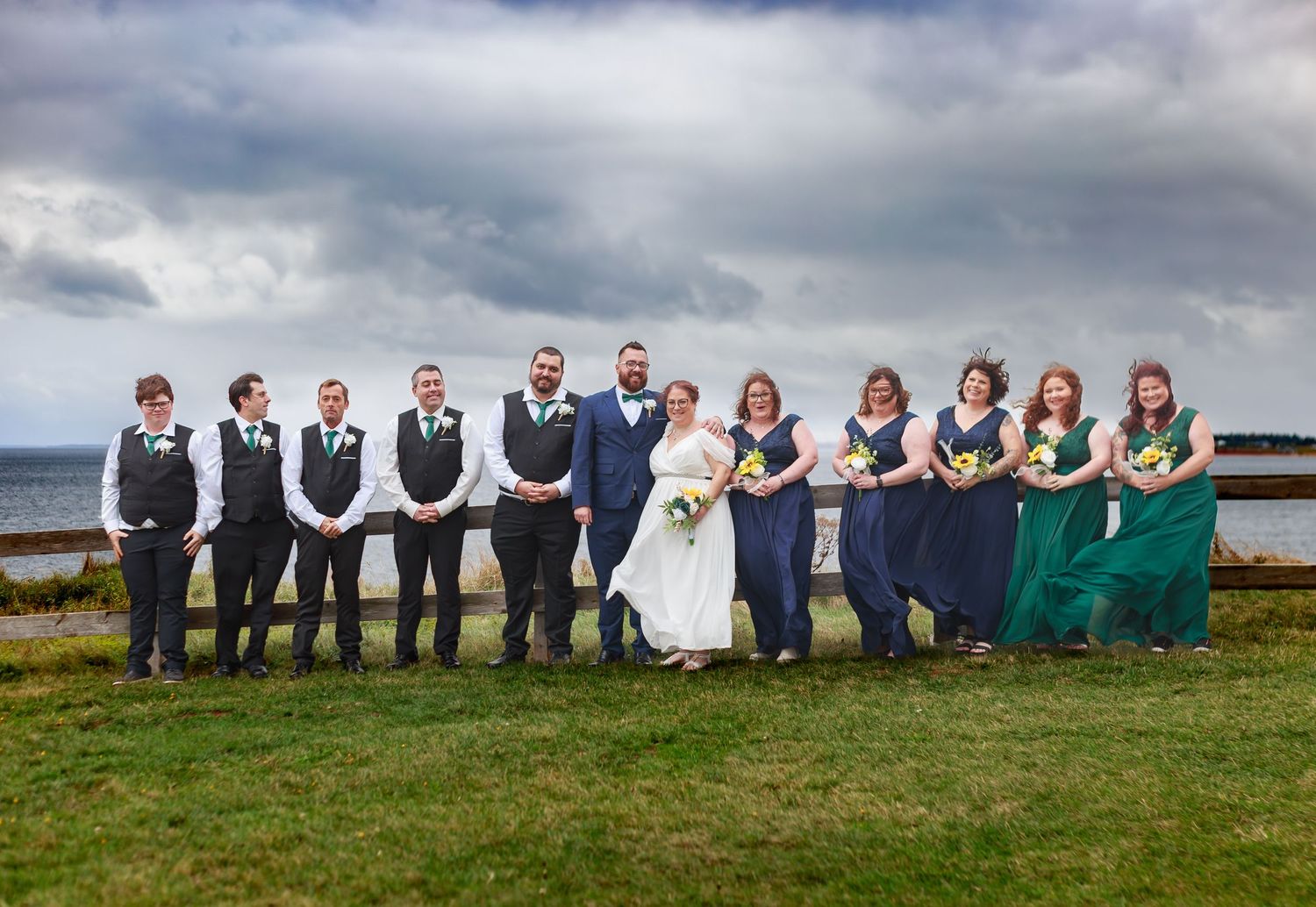 Wedding party lined up for group photos on a cloudy day by the ocean.