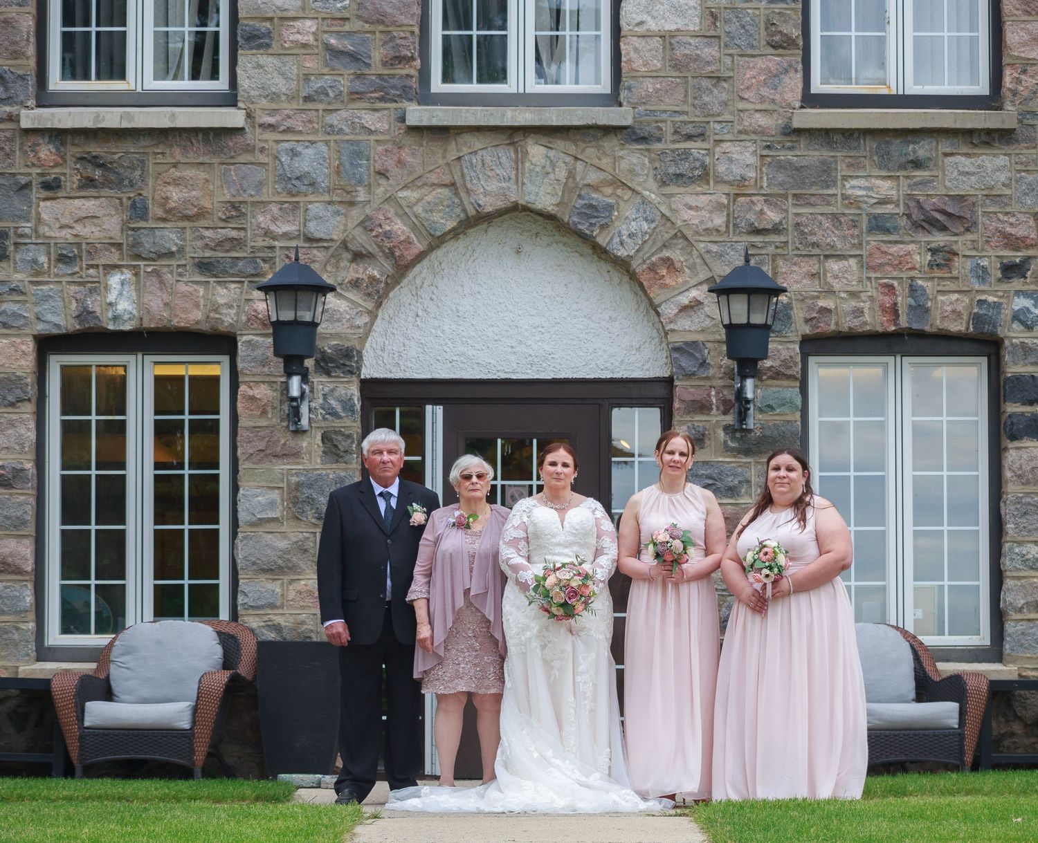 Wedding party posed in front of stone building with pink and white color scheme.