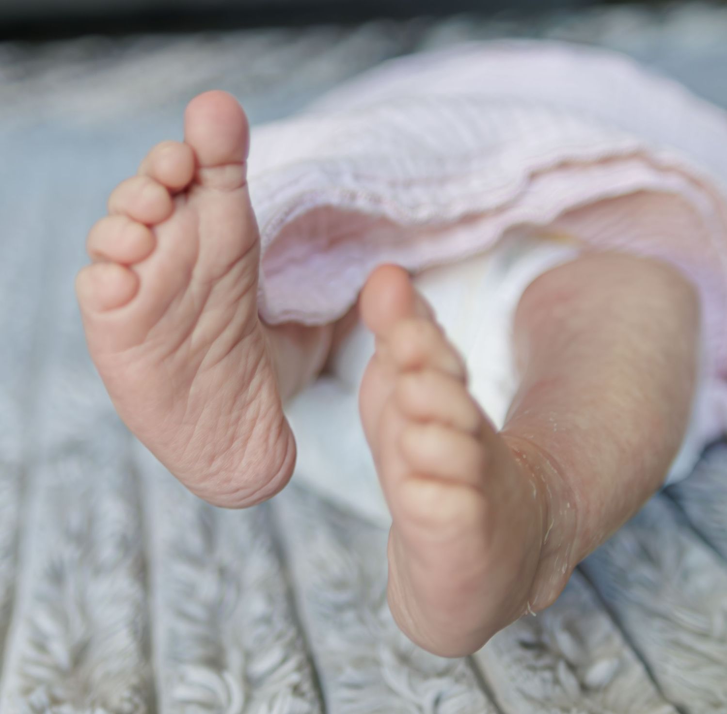 Baby feet in soft focus showing tiny toes against a textured background.