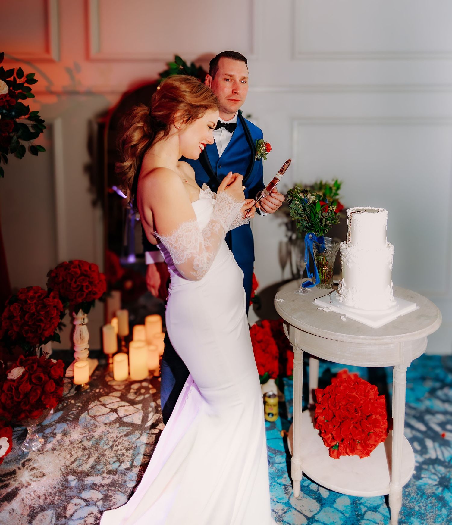 Wedding reception setup with white cake, red floral arrangements, and romantic candlelight.