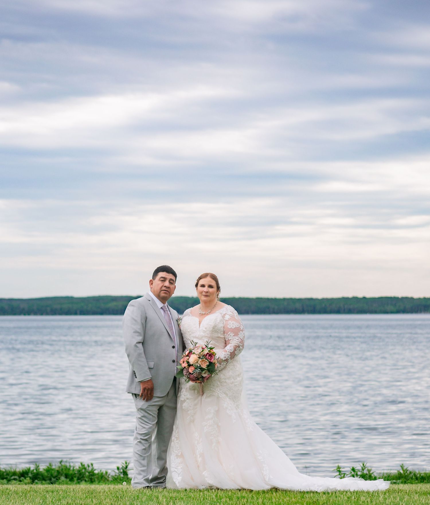 A couple in wedding attire poses together by a serene lakeside on their special day.
