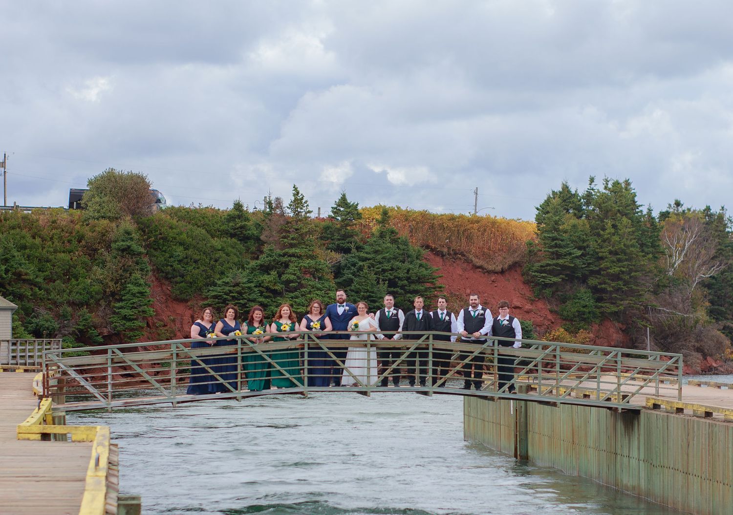 Wedding party poses on wooden boardwalk with autumn foliage in background.