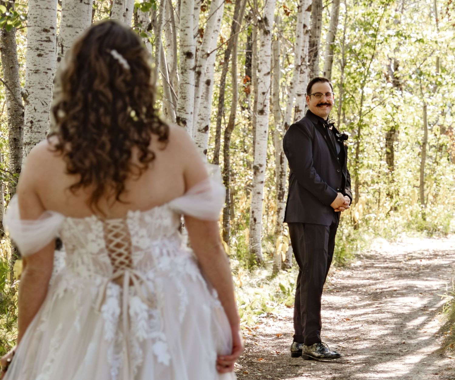 Wedding party walking through a scenic birch forest path on a sunny autumn day.