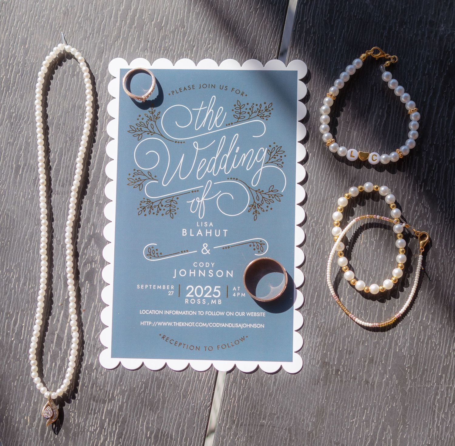 Wedding stationery and jewelry details arranged on dark surface including rings and pearl accessories.