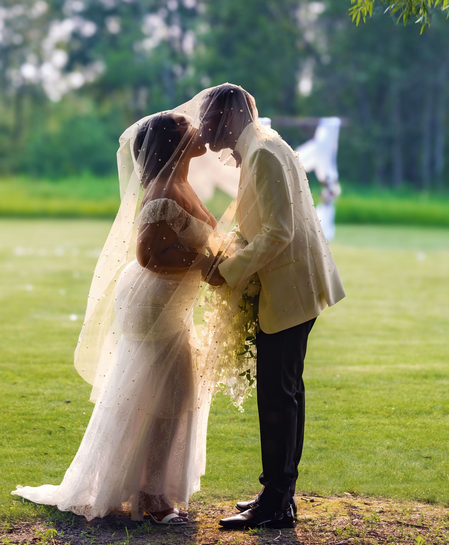 A romantic wedding couple shares intimate moments in a lush green field.