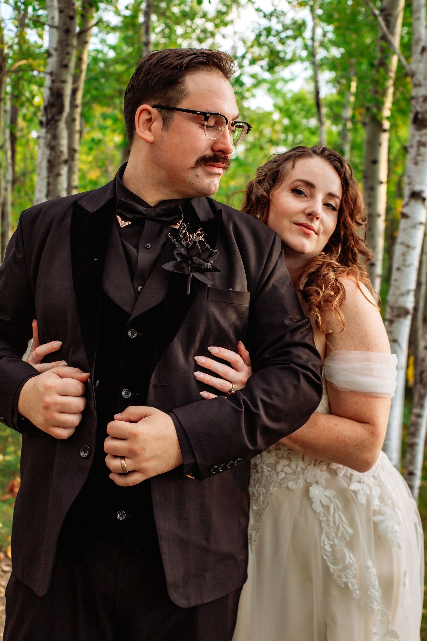 A couple in wedding attire poses together in a birch forest.