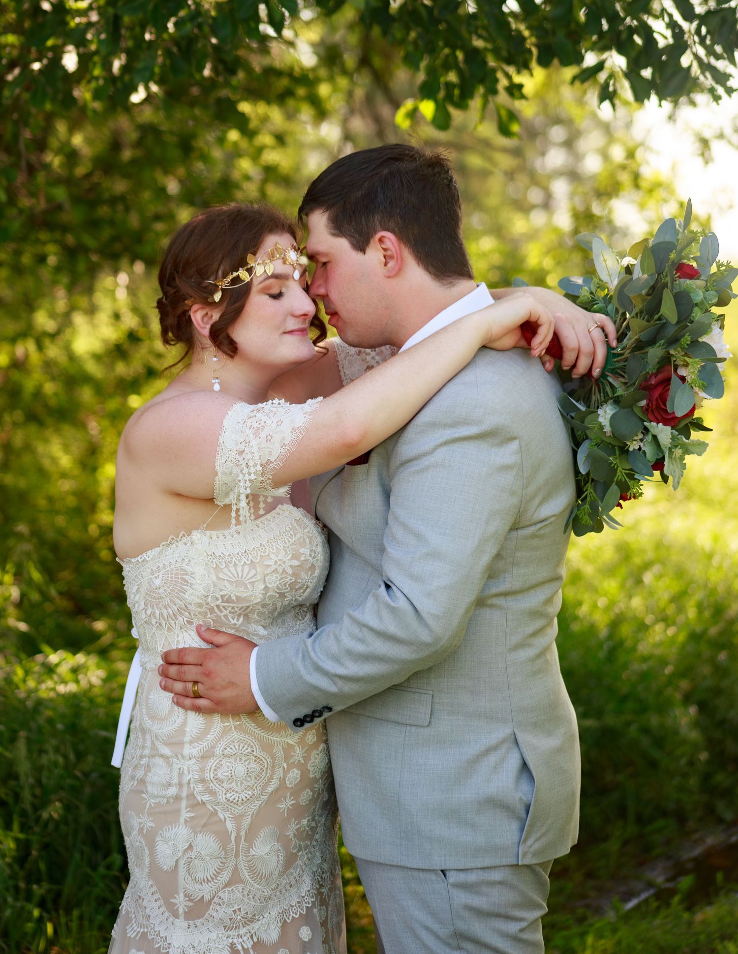 A tender moment between newlyweds surrounded by lush greenery and golden sunlight.