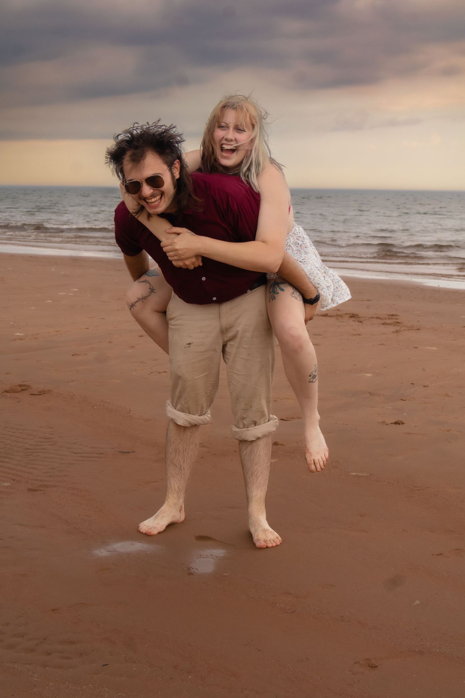 A playful couple having fun on a cloudy beach with bare feet in the sand.