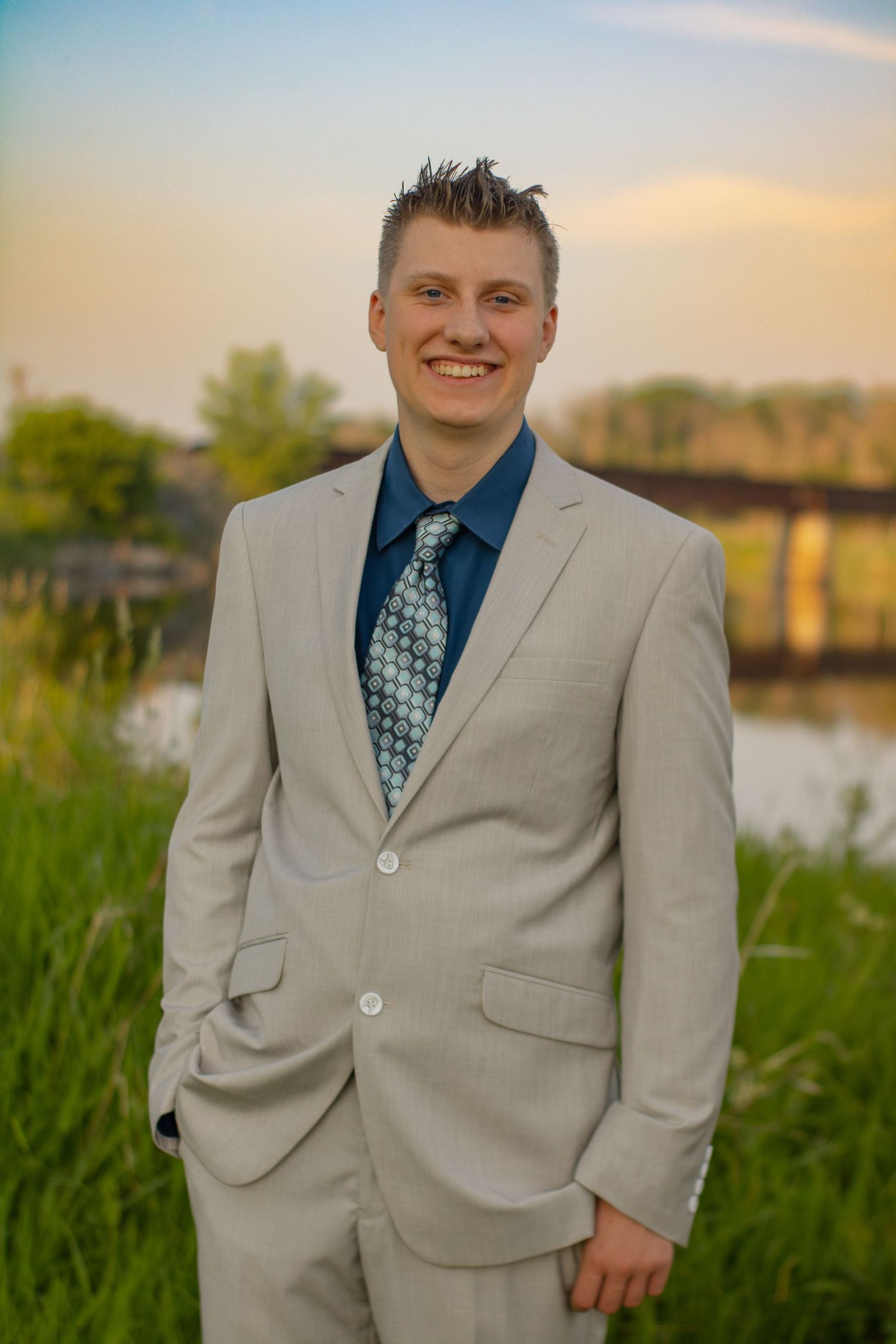 Professional portrait in light gray suit and patterned tie by a lakeside setting.