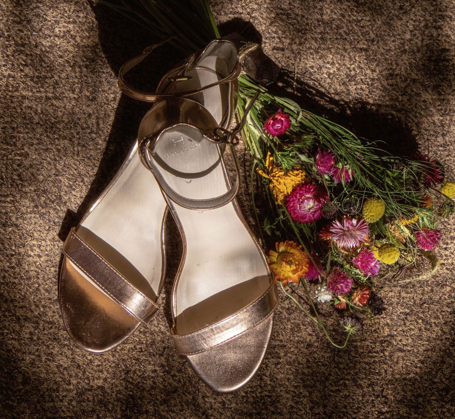 Wedding shoes and colorful wildflower bouquet arranged on dark textured background.