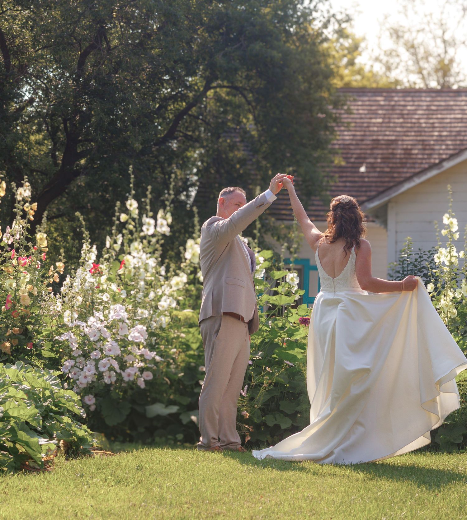 Couple dancing joyfully in a sunlit garden with white flowers in the background.