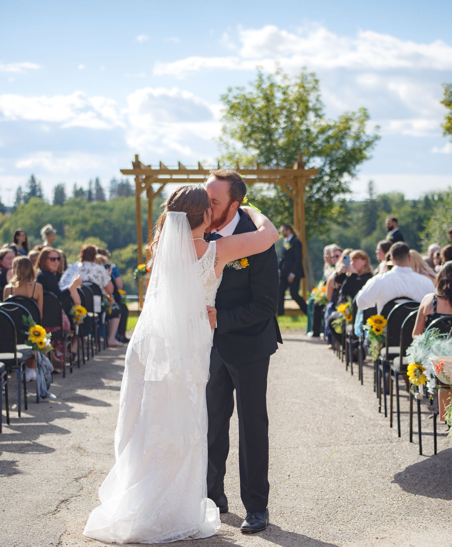 Outdoor wedding ceremony setup with white chairs and sunflower decorations along the aisle.