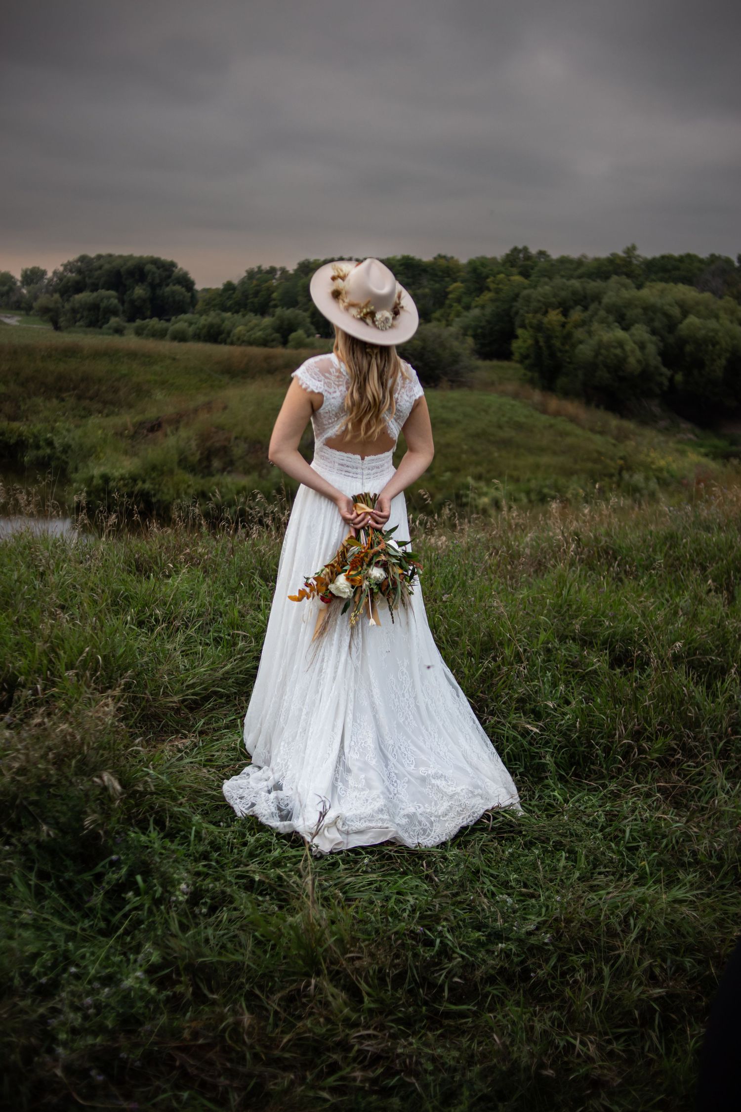 White lace wedding dress photographed in a grassy field during golden hour.