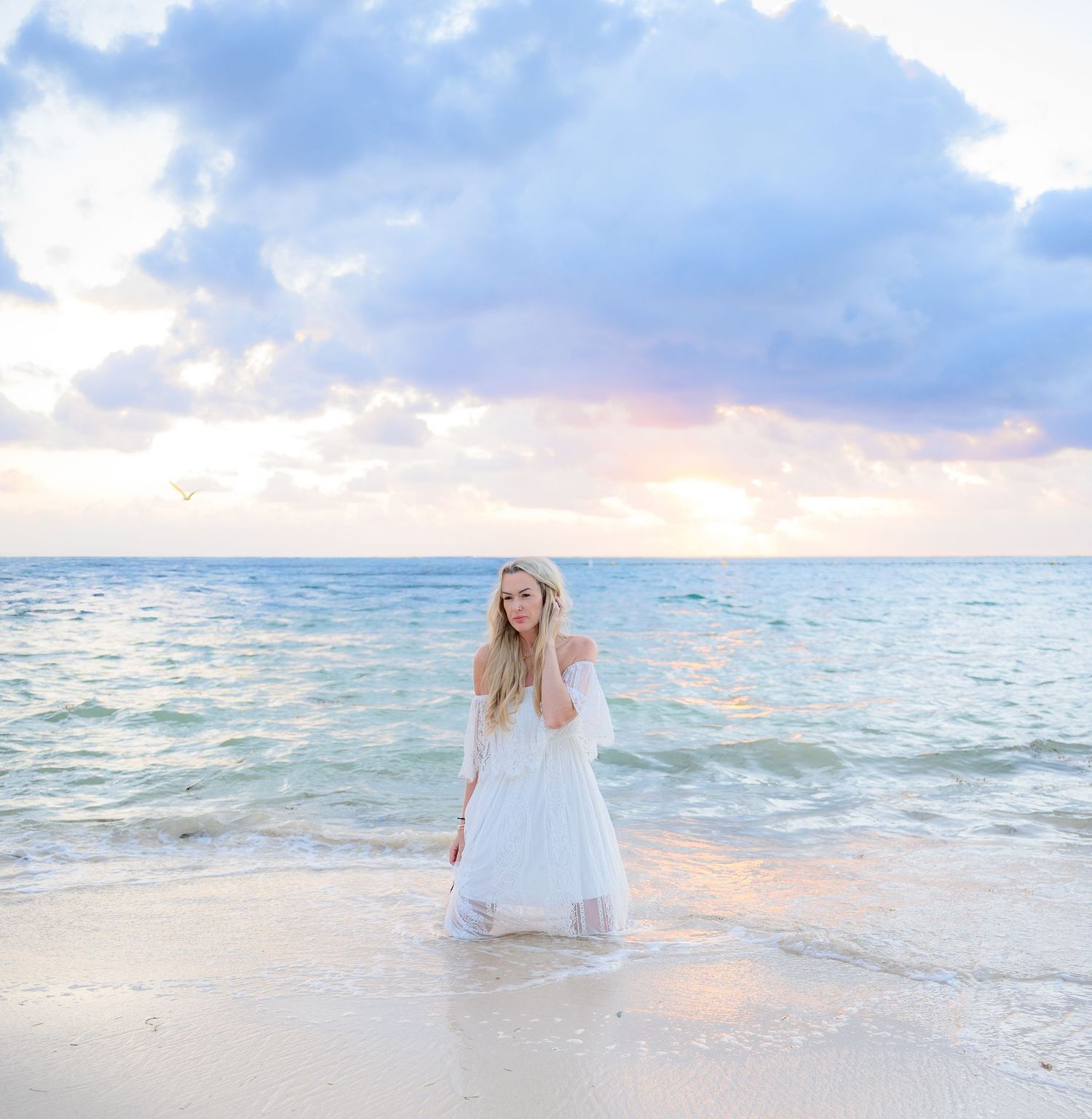 A white flowy dress catches the ocean breeze during a dreamy beach sunset photoshoot.