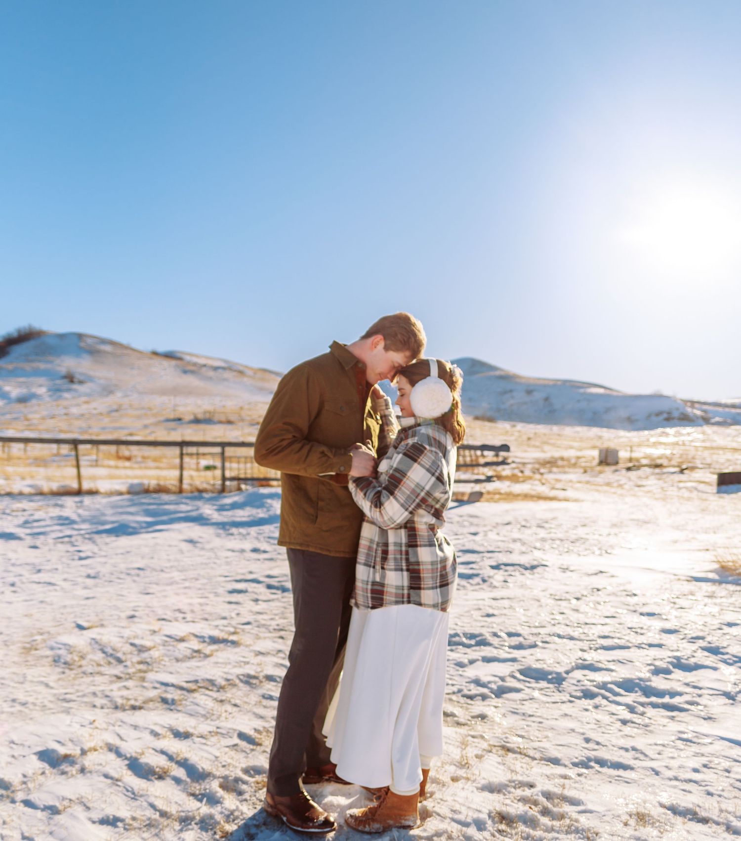 A romantic moment captured in a snowy field with mountains on the horizon.