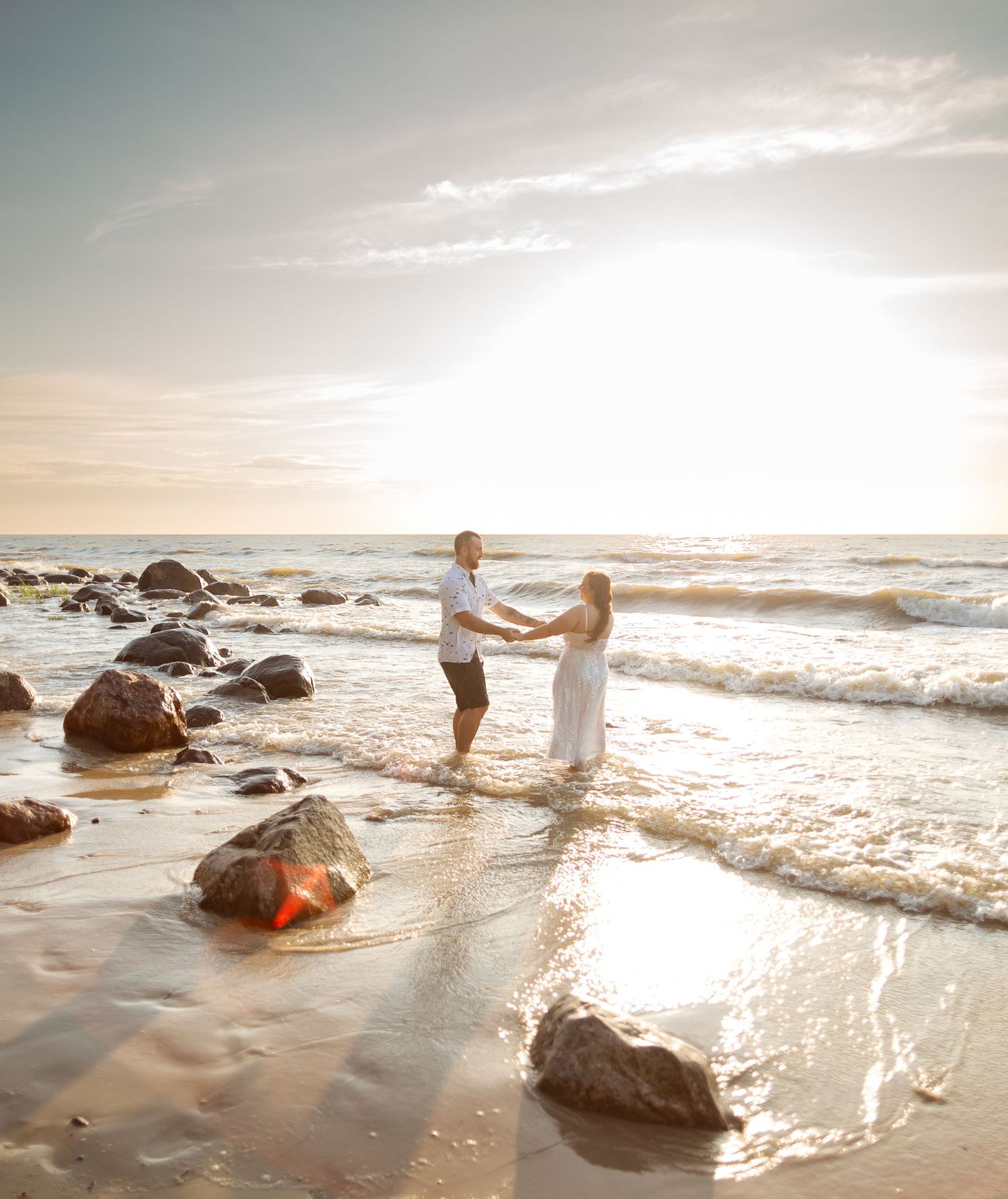 Romantic beach photoshoot with waves splashing against rocks at golden hour.