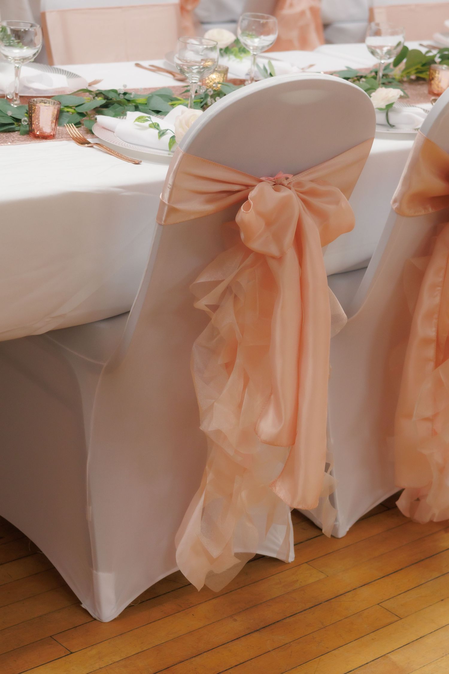 Wedding reception chairs decorated with peach-colored bows and white covers.