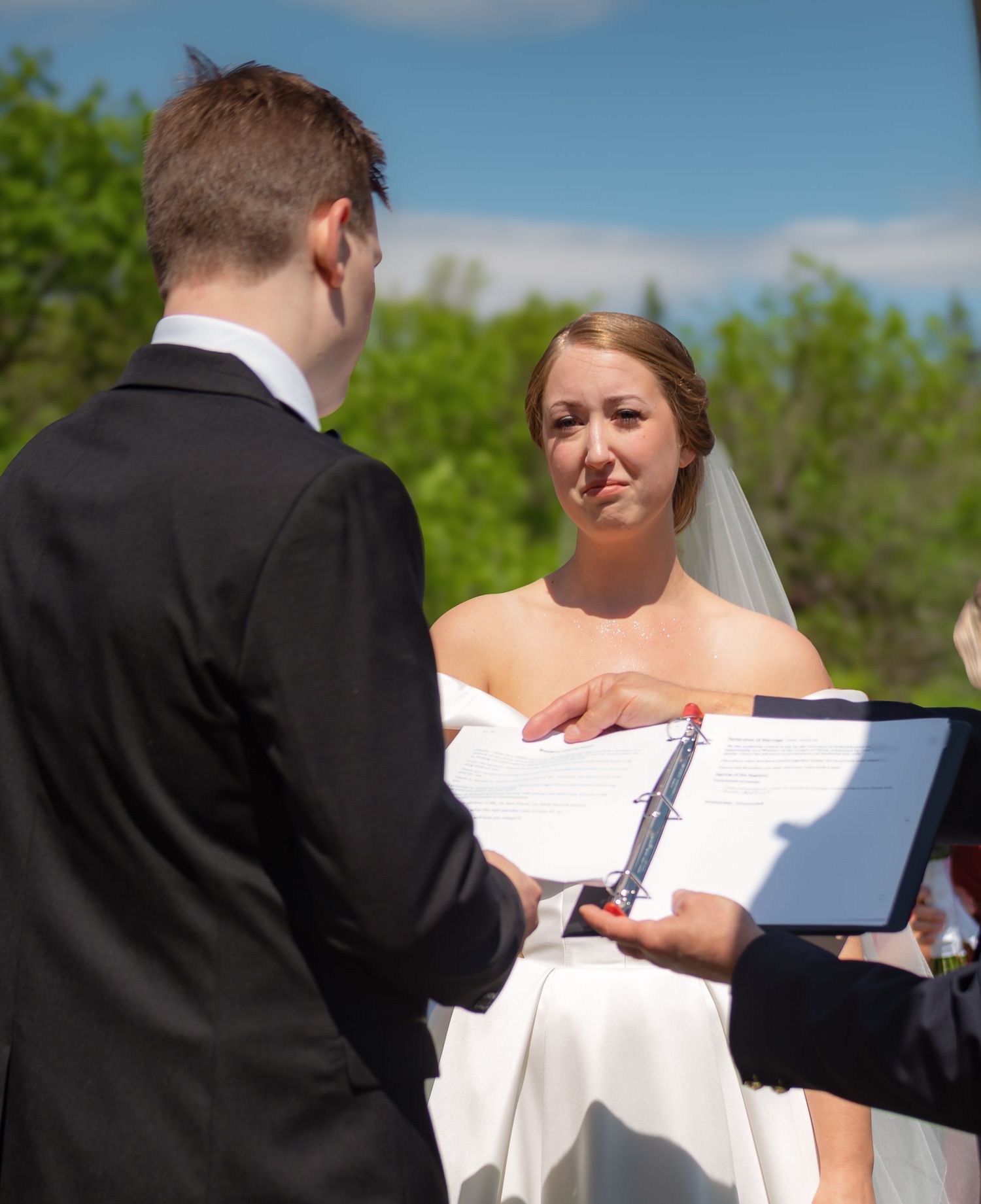Couple exchanging vows and reading from ceremony cards during outdoor wedding ceremony.